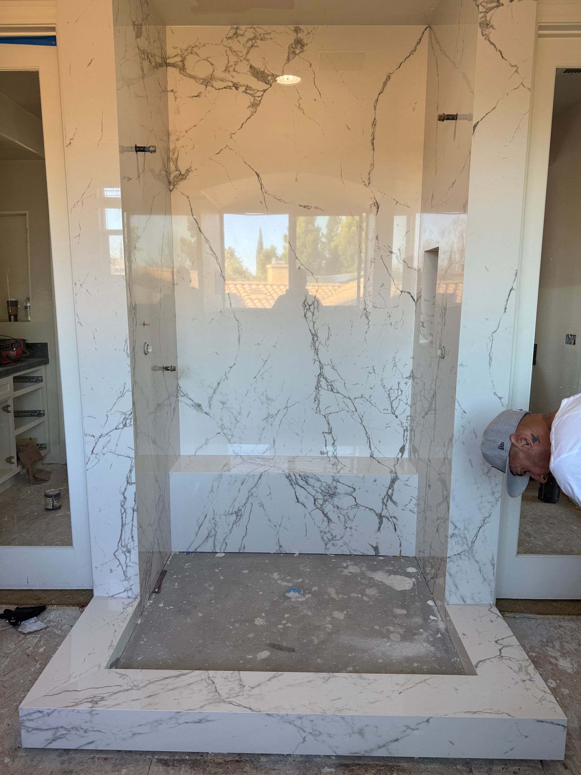 Bathroom shower enclosure with marble tile, glass, and a person working.