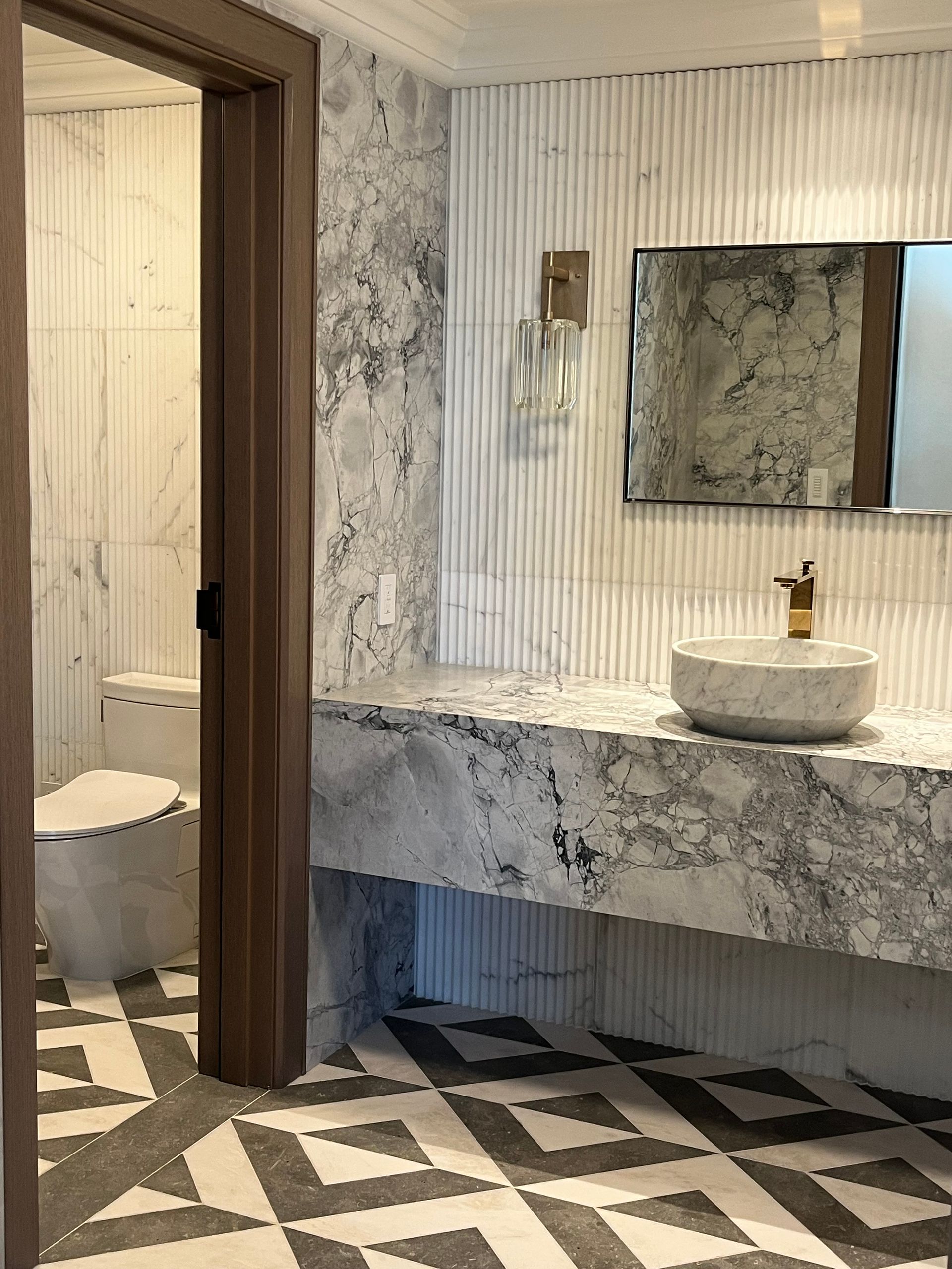 Luxurious bathroom with marble countertop, patterned floor, and open door to a toilet.