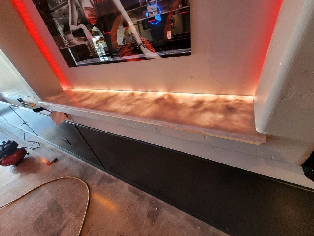 Shelf with red LED lighting, above a cabinet. A framed picture hangs on the wall.