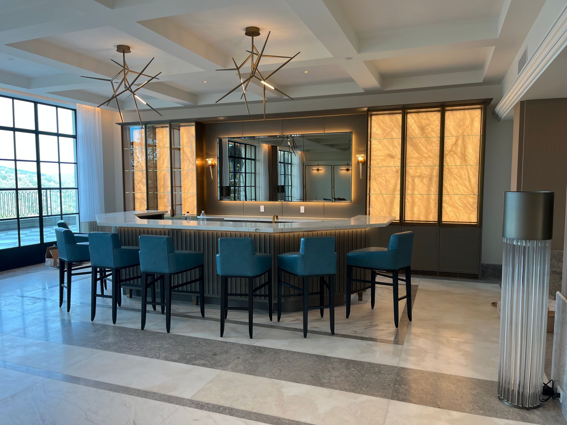 A stylish bar area with blue barstools, a large mirror, and decorative lighting in a luxury setting.
