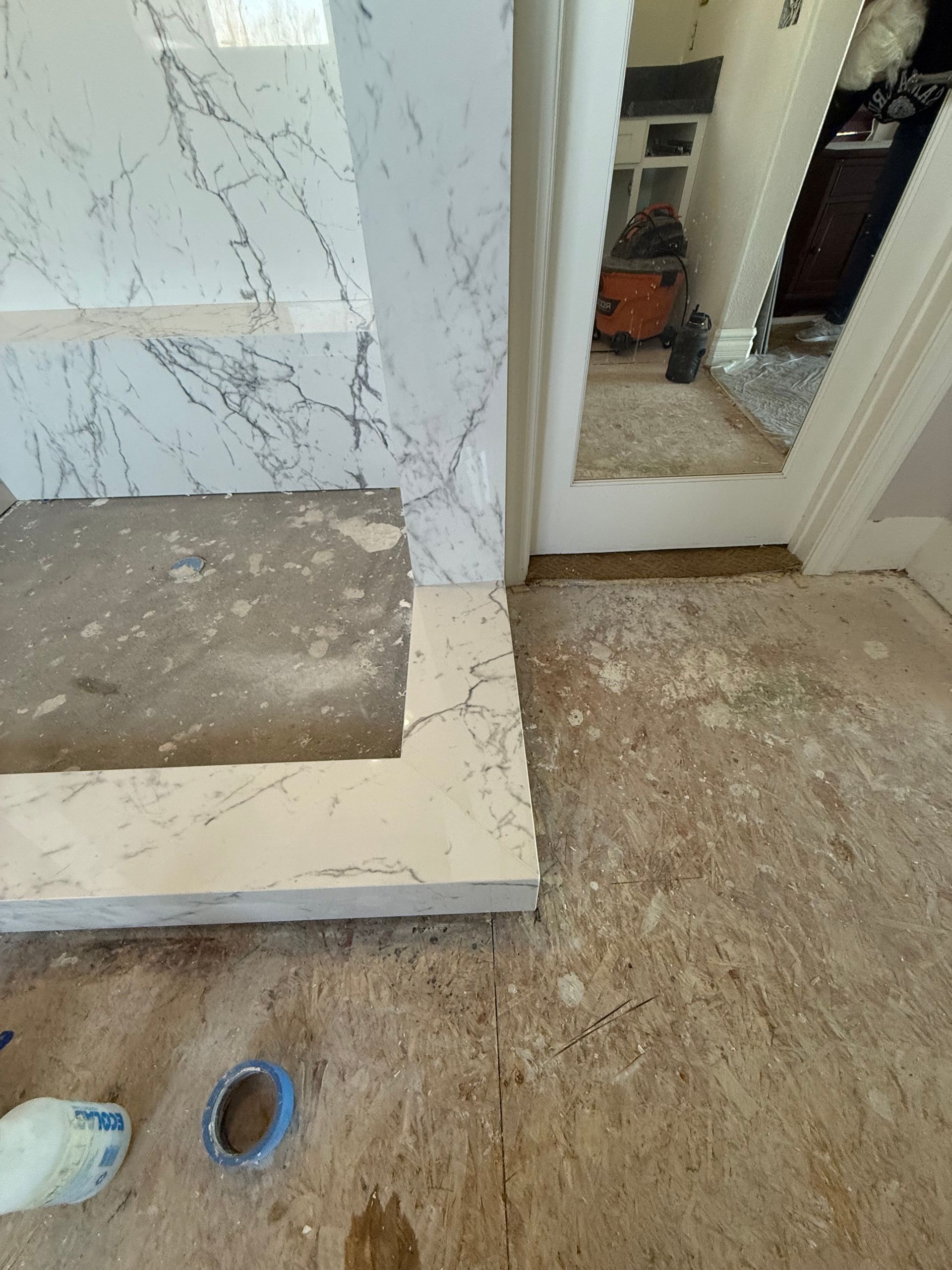 Bathroom remodel: Marble tile edging around a step-up area and doorway. Rough concrete floors visible.