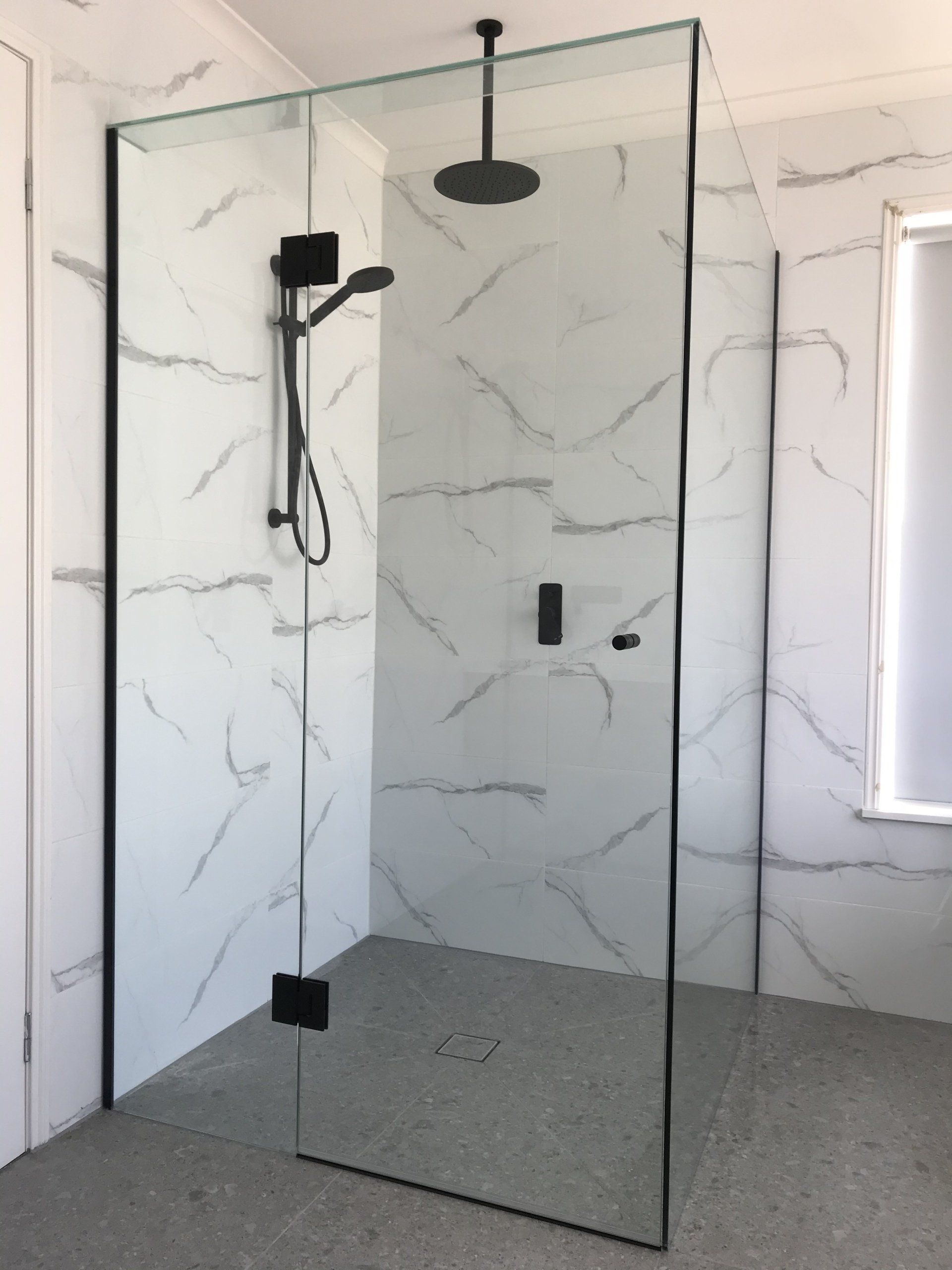 A bathroom with a walk in Frameless Hinged Shower Screen with a black shower head.