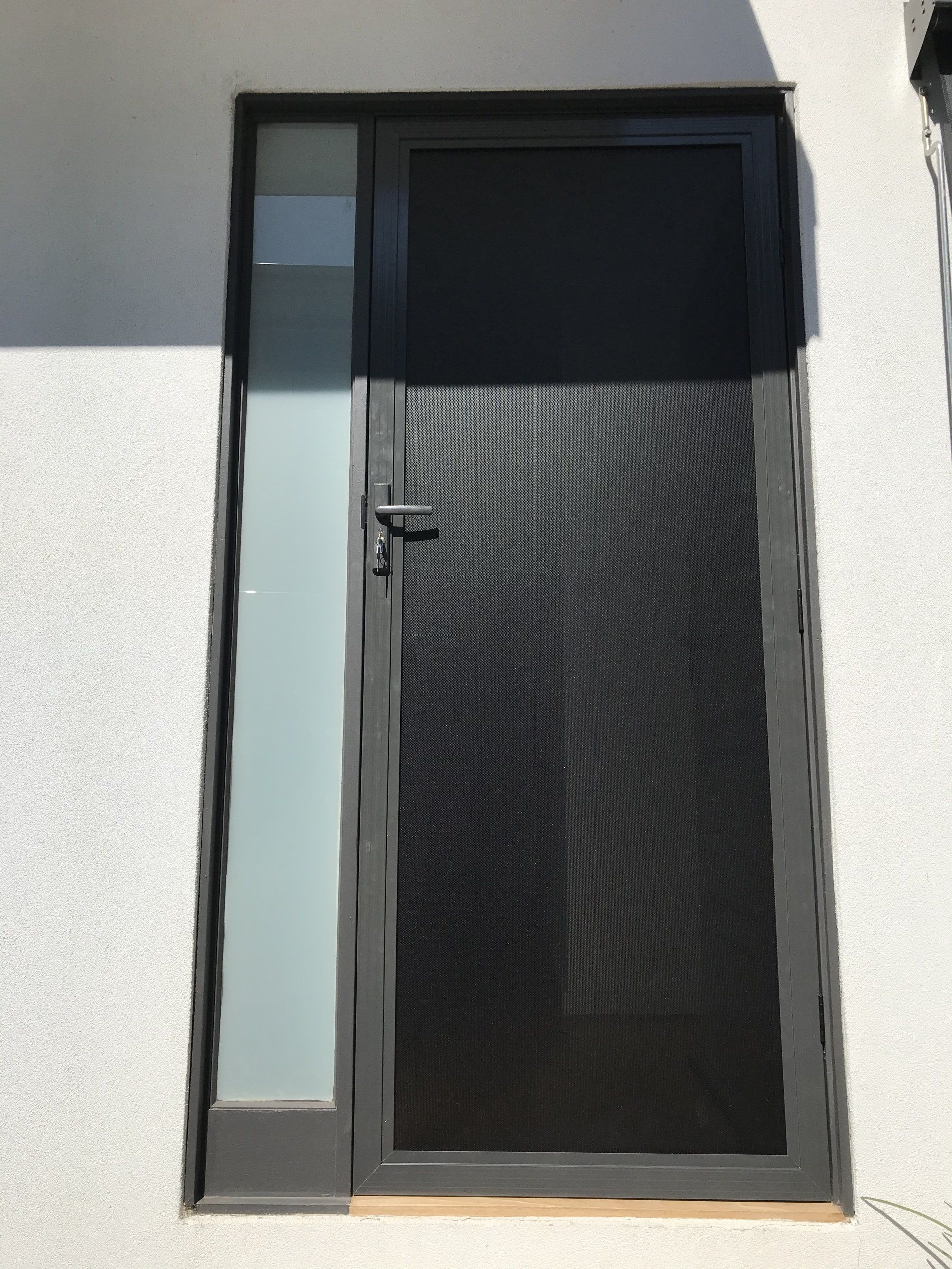 A black Security Door with a screen on it is on a white wall