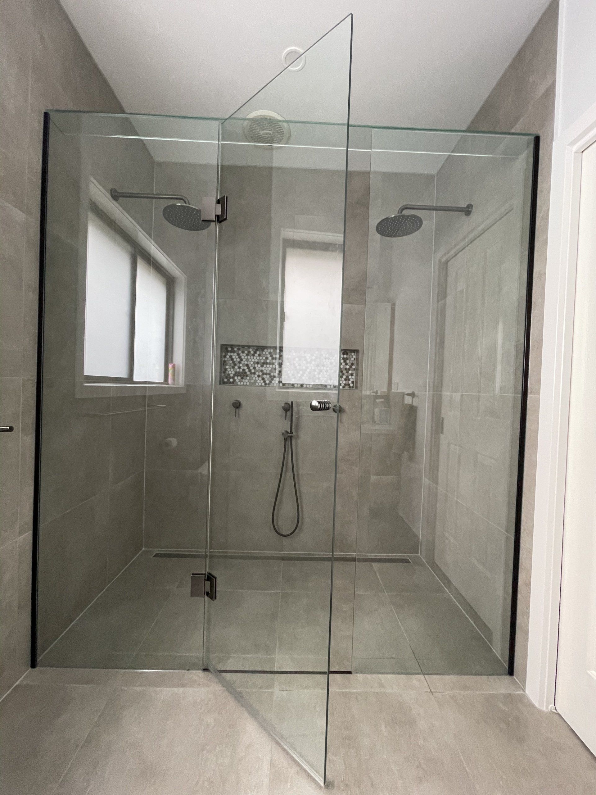 A bathroom with a walk in Frameless Hinged Shower Screen with a glass door.