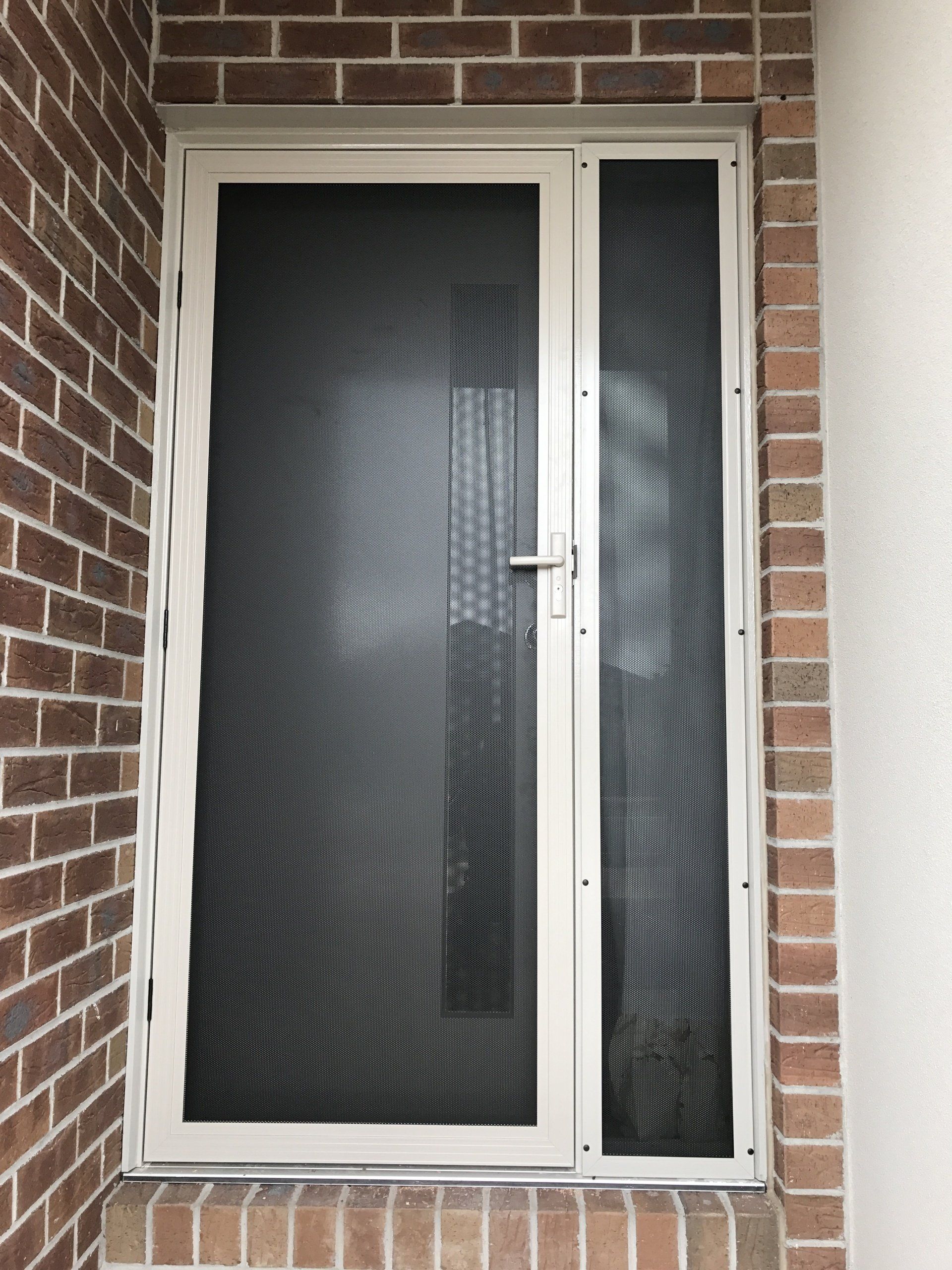 A white screen door is on a brick wall.
