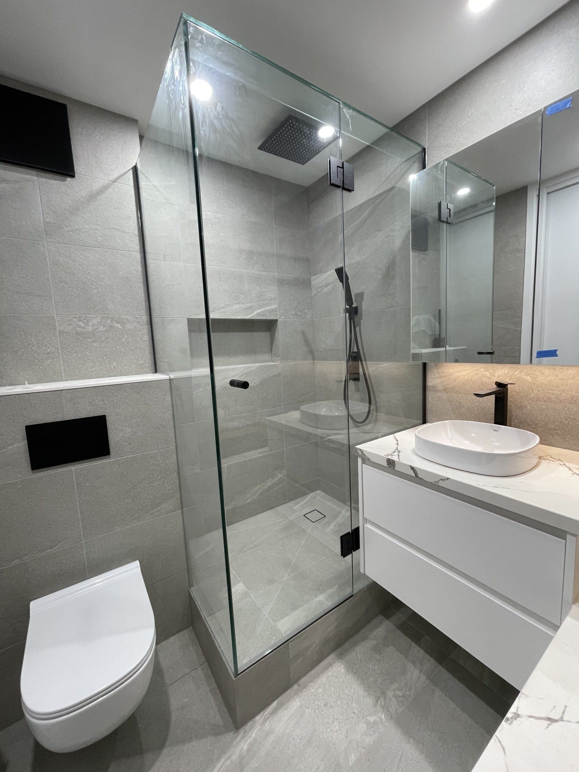 A bathroom with a walk in Frameless Hinged Shower Screen , sink , toilet and mirror.
