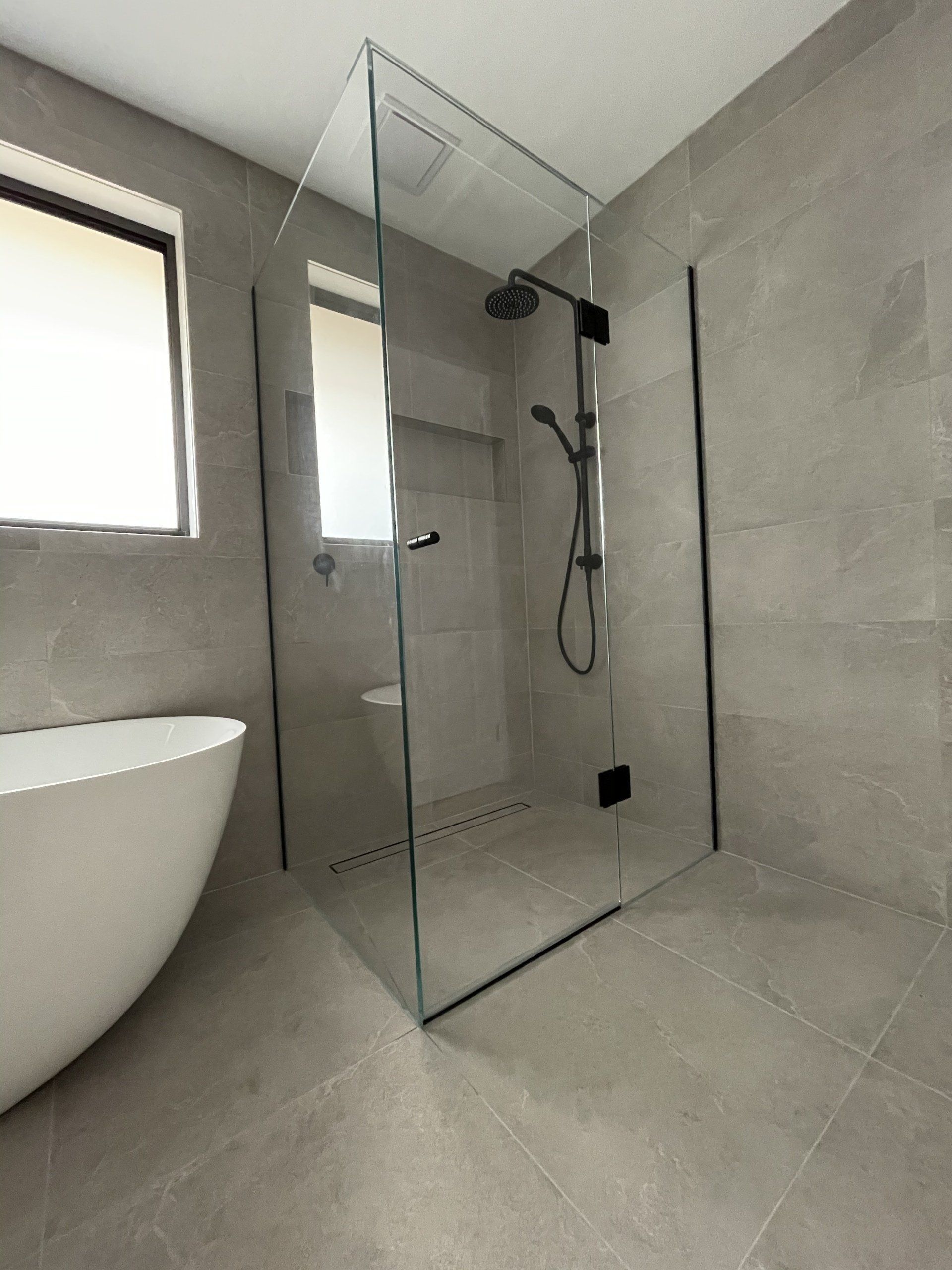 A bathroom with a walk in Frameless Hinged Shower Screen and a bathtub.