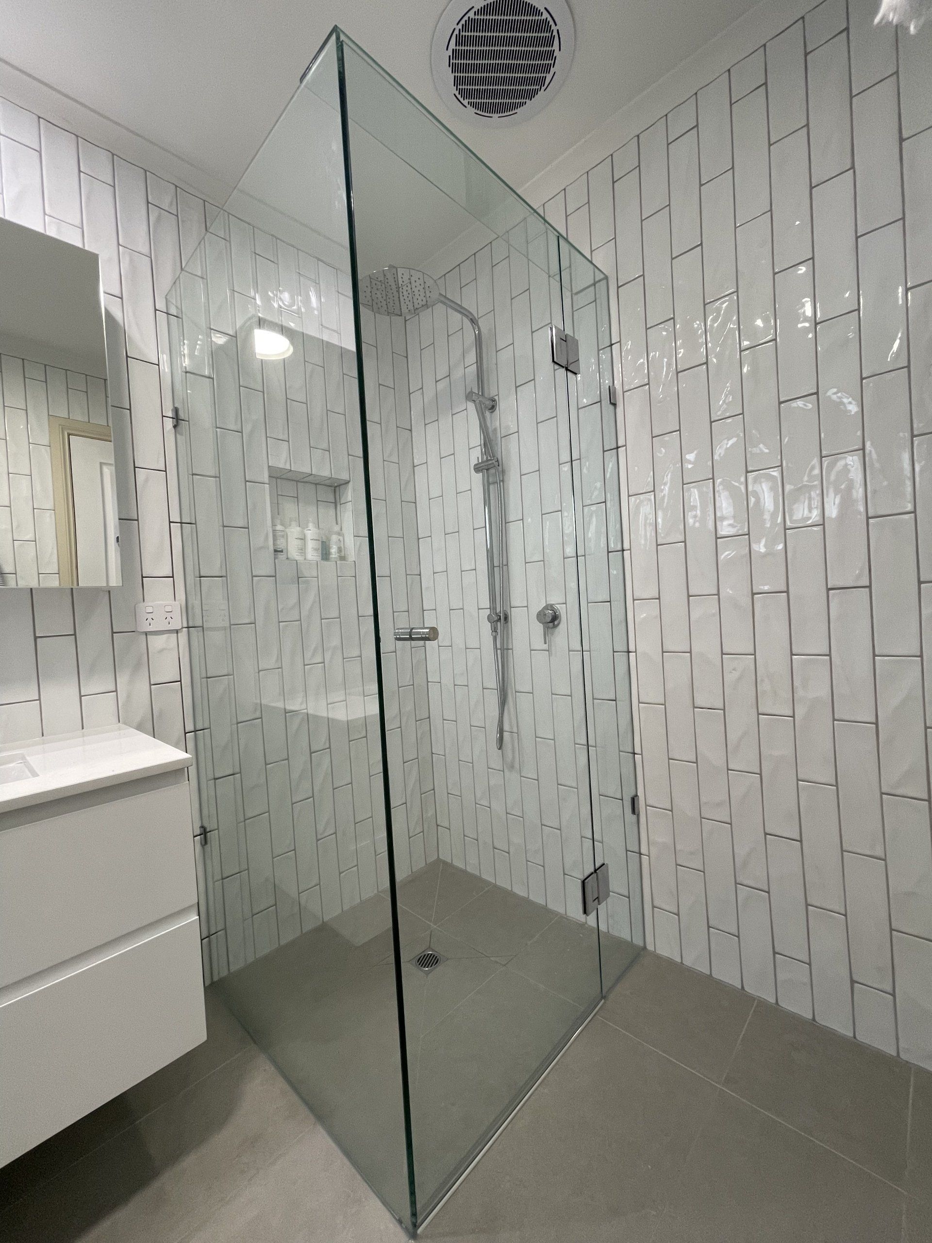 A bathroom with a walk in Frameless Hinged Shower Screen and a sink.