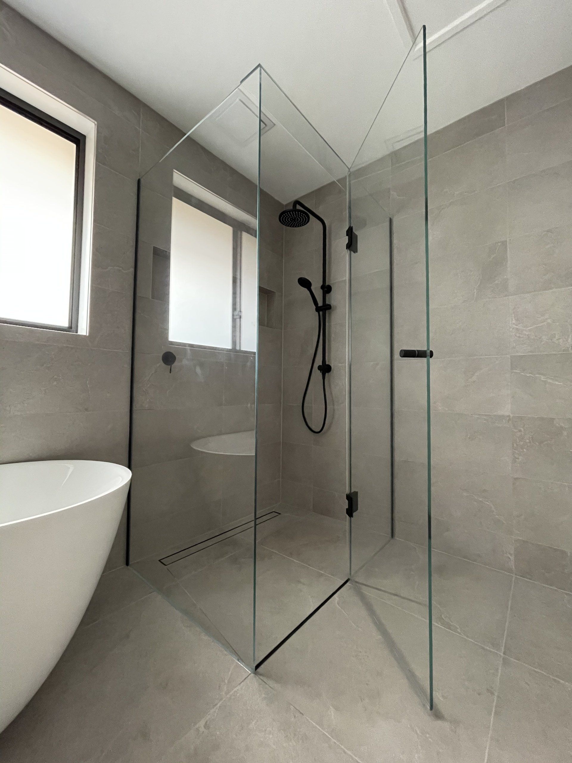 A bathroom with a walk in Frameless Hinged Shower Screen and a bathtub