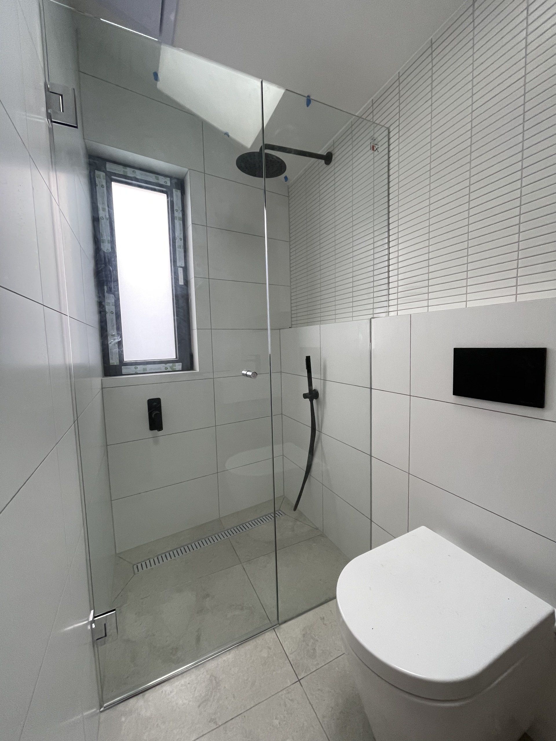 A bathroom with a toilet a Frameless Hinged Shower Screen and a window
