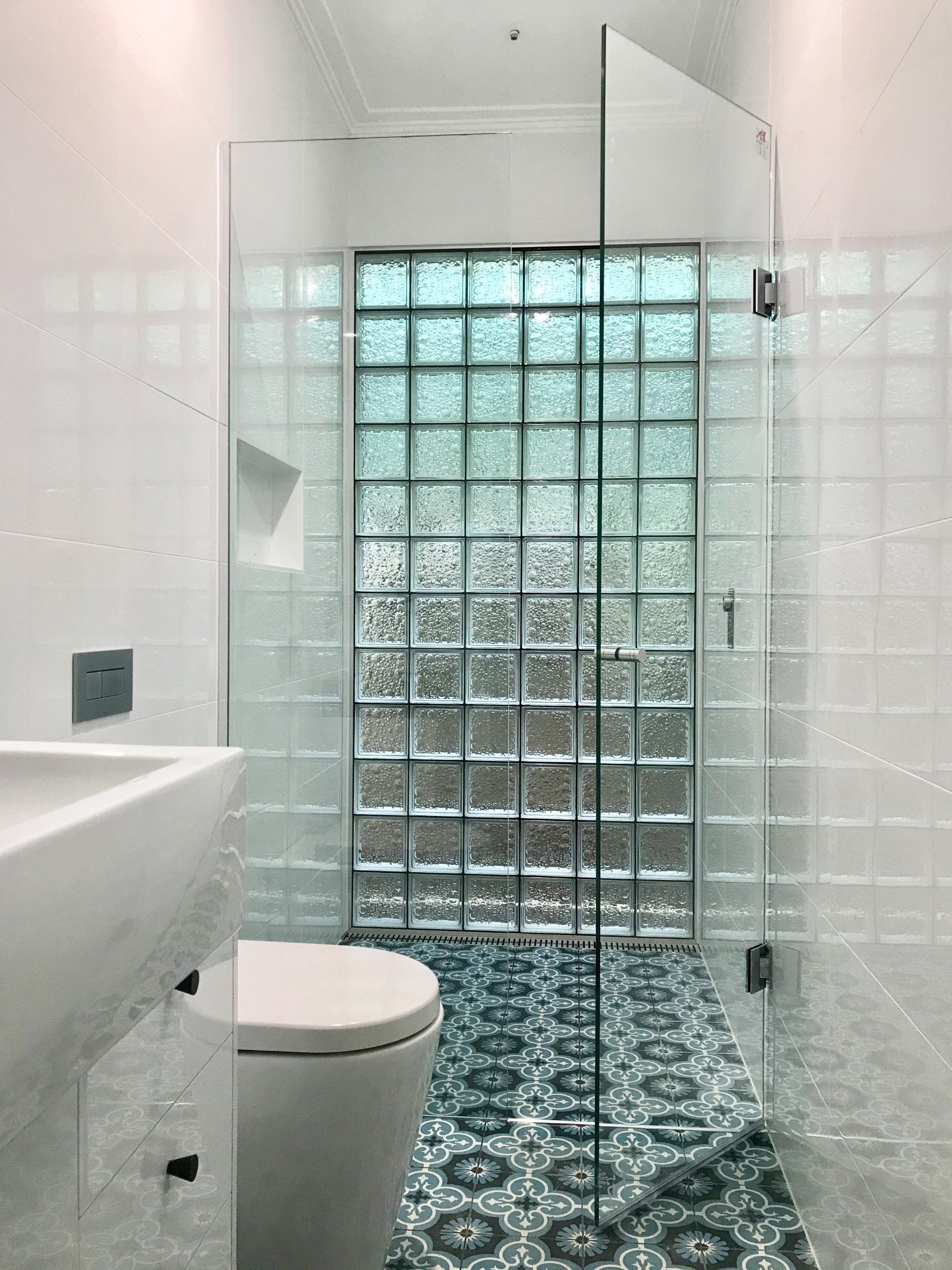 A bathroom with a toilet , sink , shower and glass blocks.