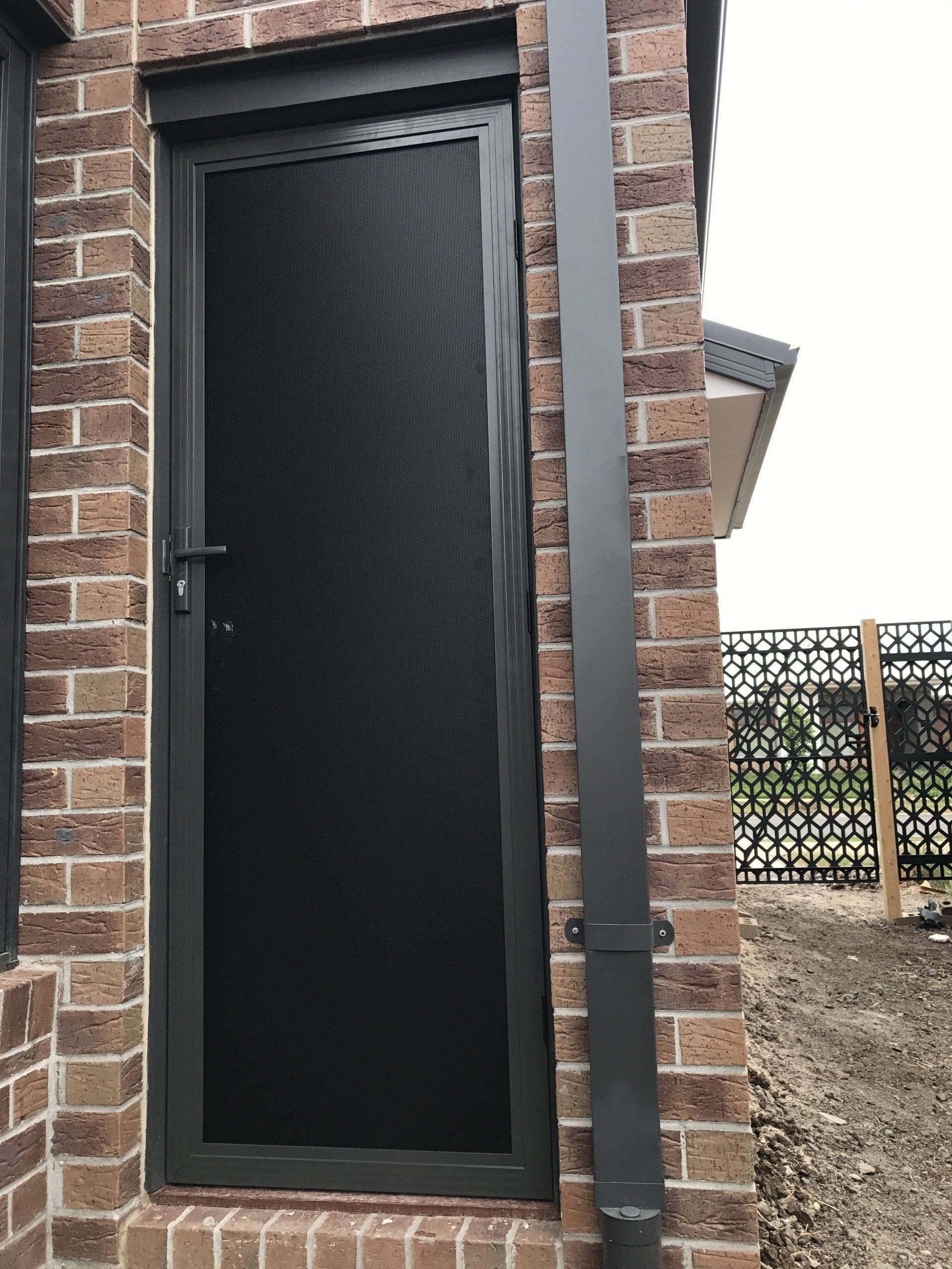 A black door is sitting on a brick wall next to a drain pipe.