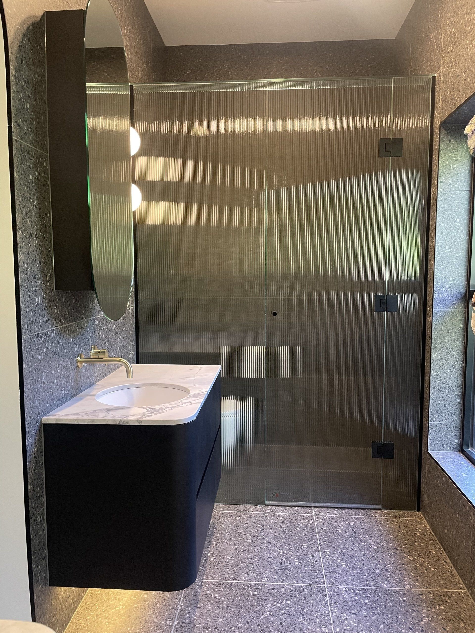 A bathroom with a sink and a walk in Frameless Hinged Shower Screens