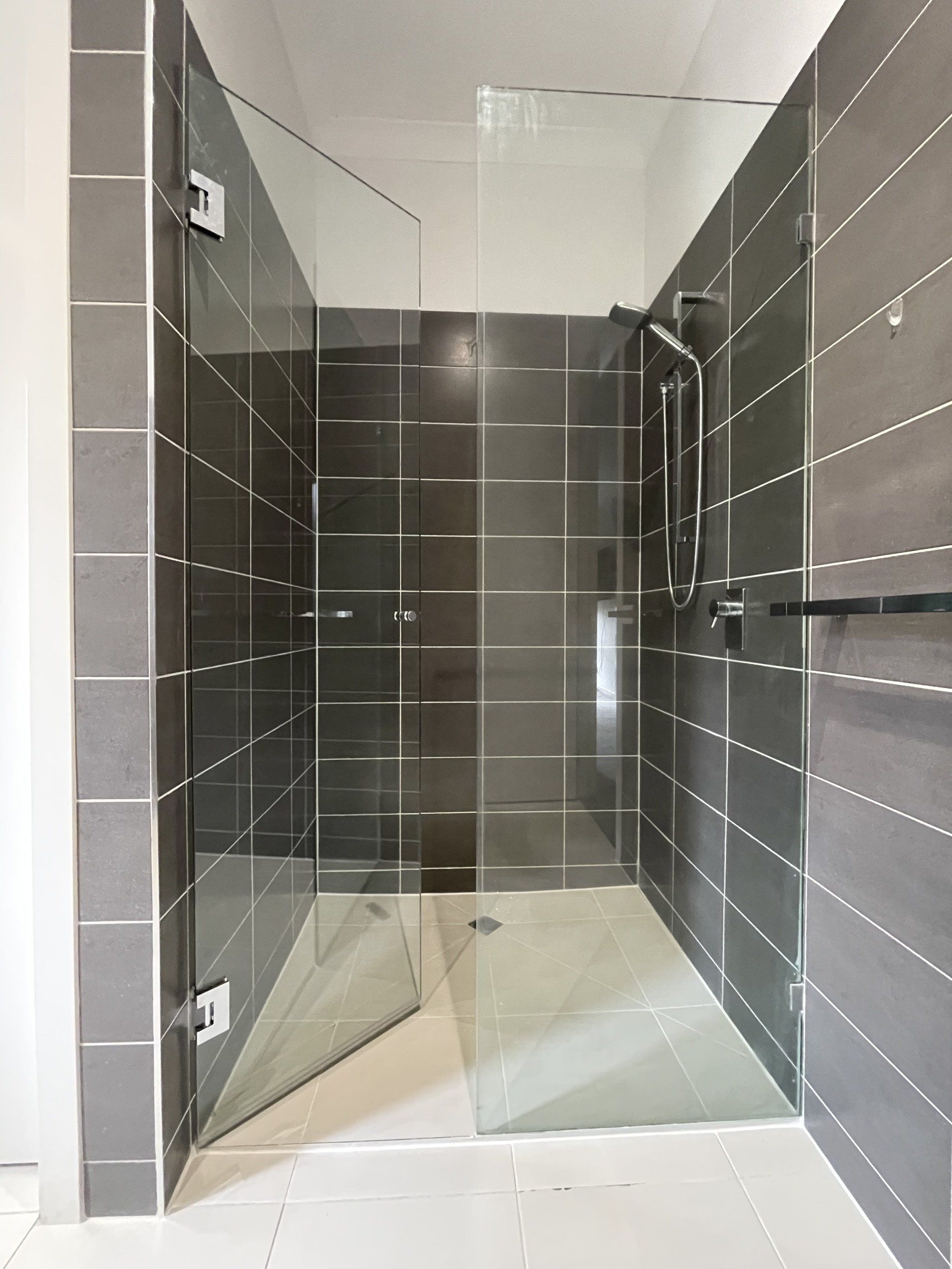 A bathroom with a walk in Frameless Hinged Shower Screen with a glass door