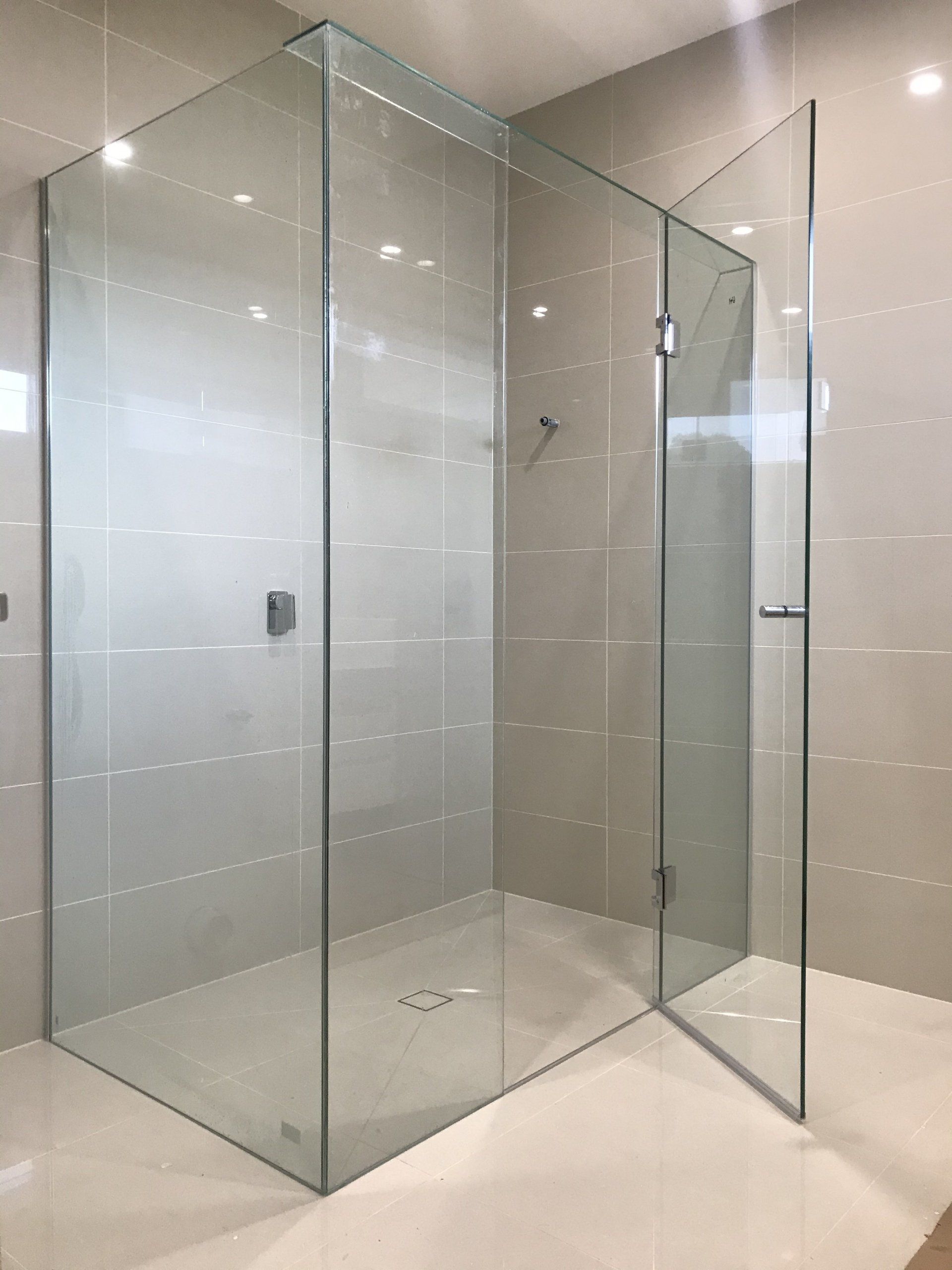 A bathroom with a walk in Frameless Hinged Shower Screen with a glass door.