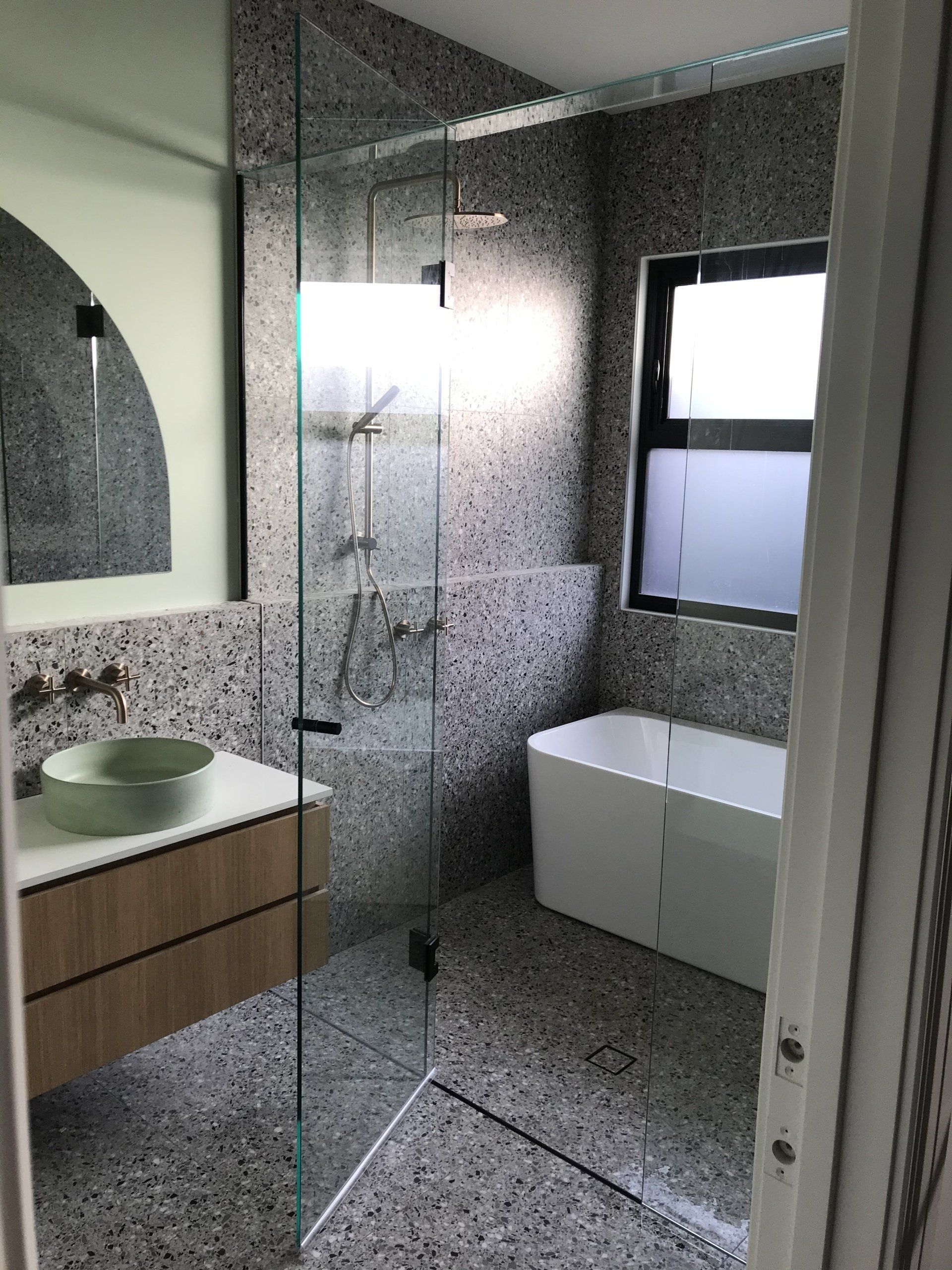 A bathroom with a bathtub , sink , Frameless Hinged Shower Screen and mirror.