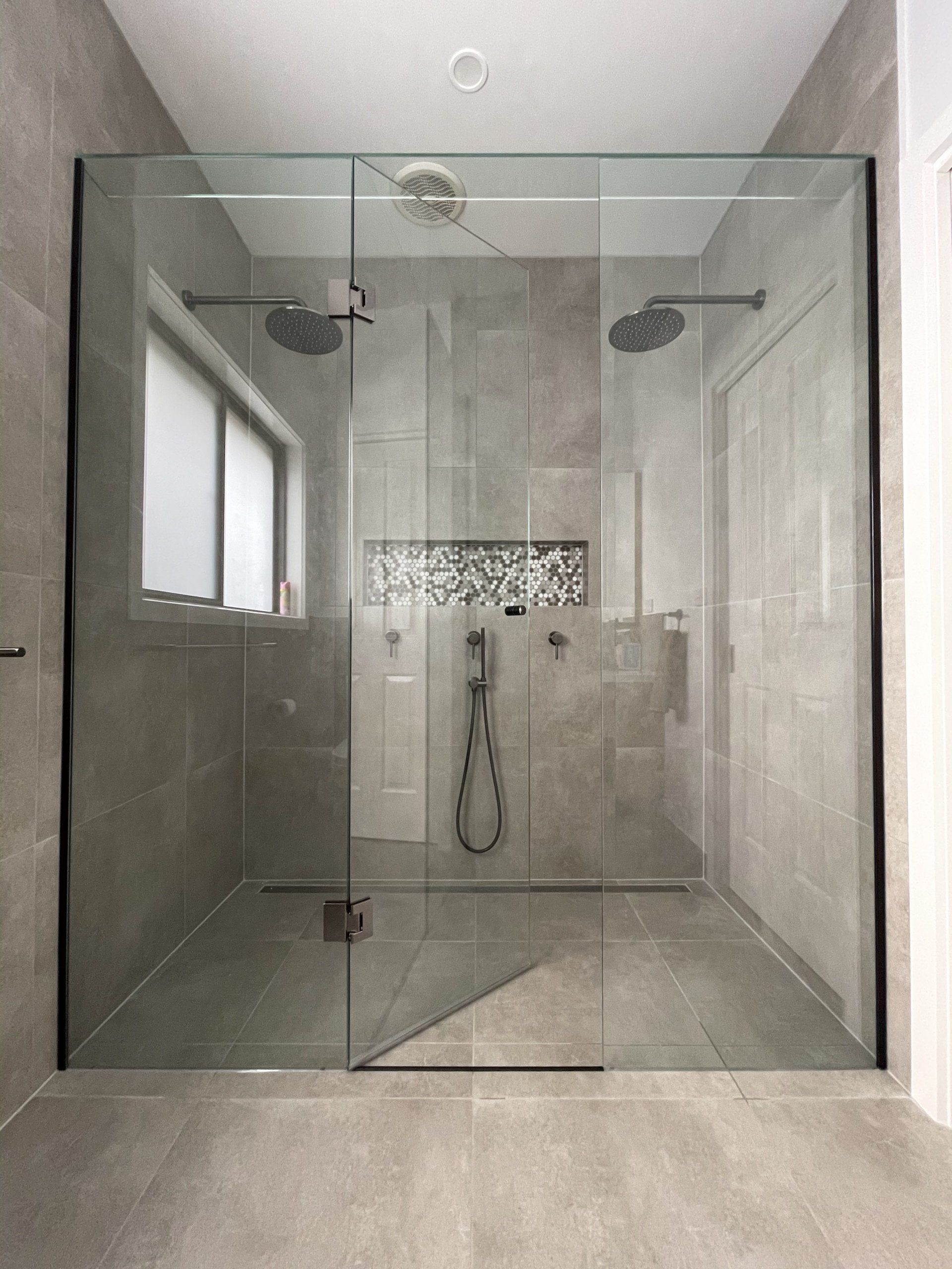 A bathroom with a walk in Frameless Hinged Shower Screen with a glass door.