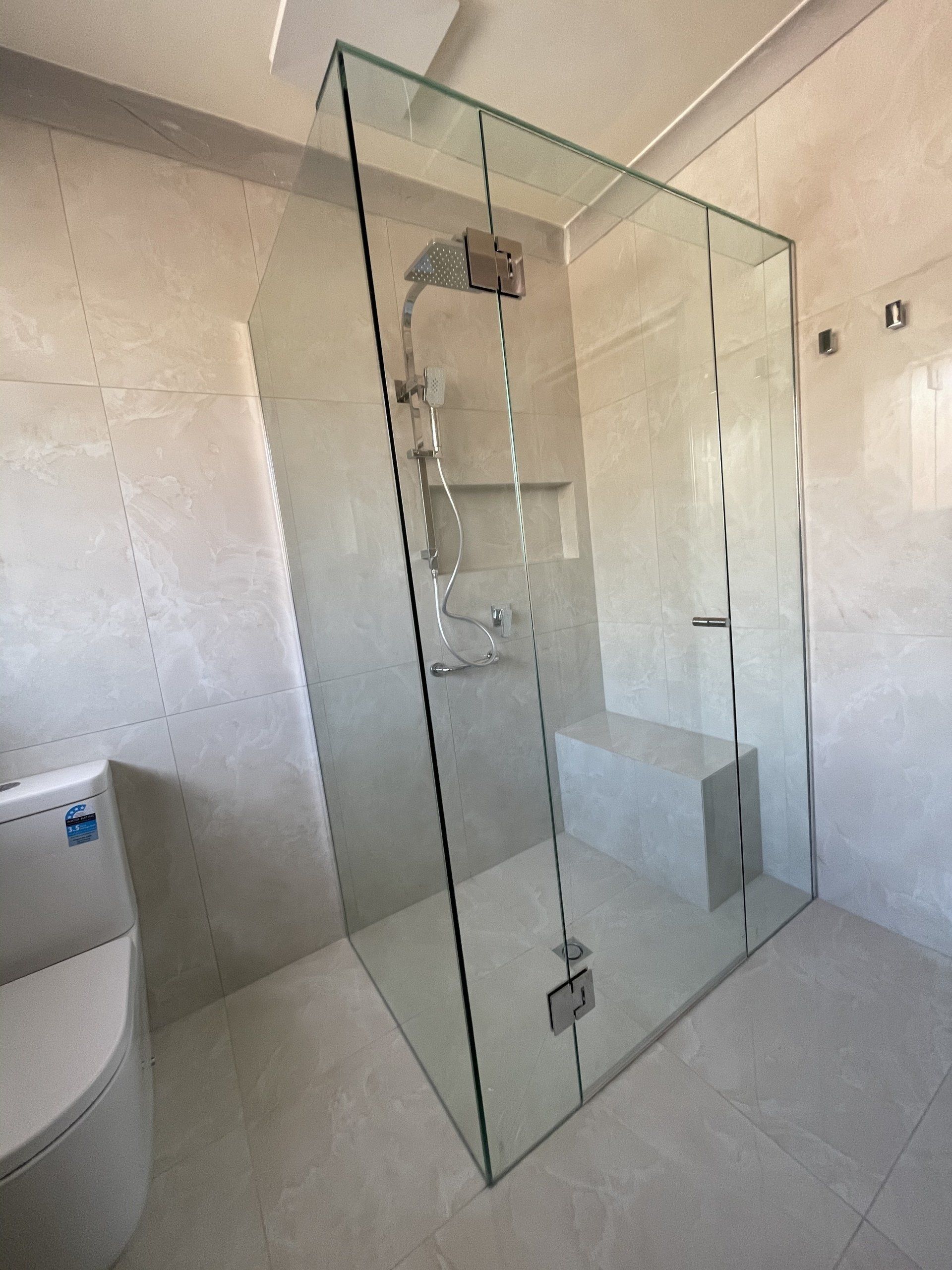 A bathroom with a toilet and a walk in Frameless Hinged Shower Screen