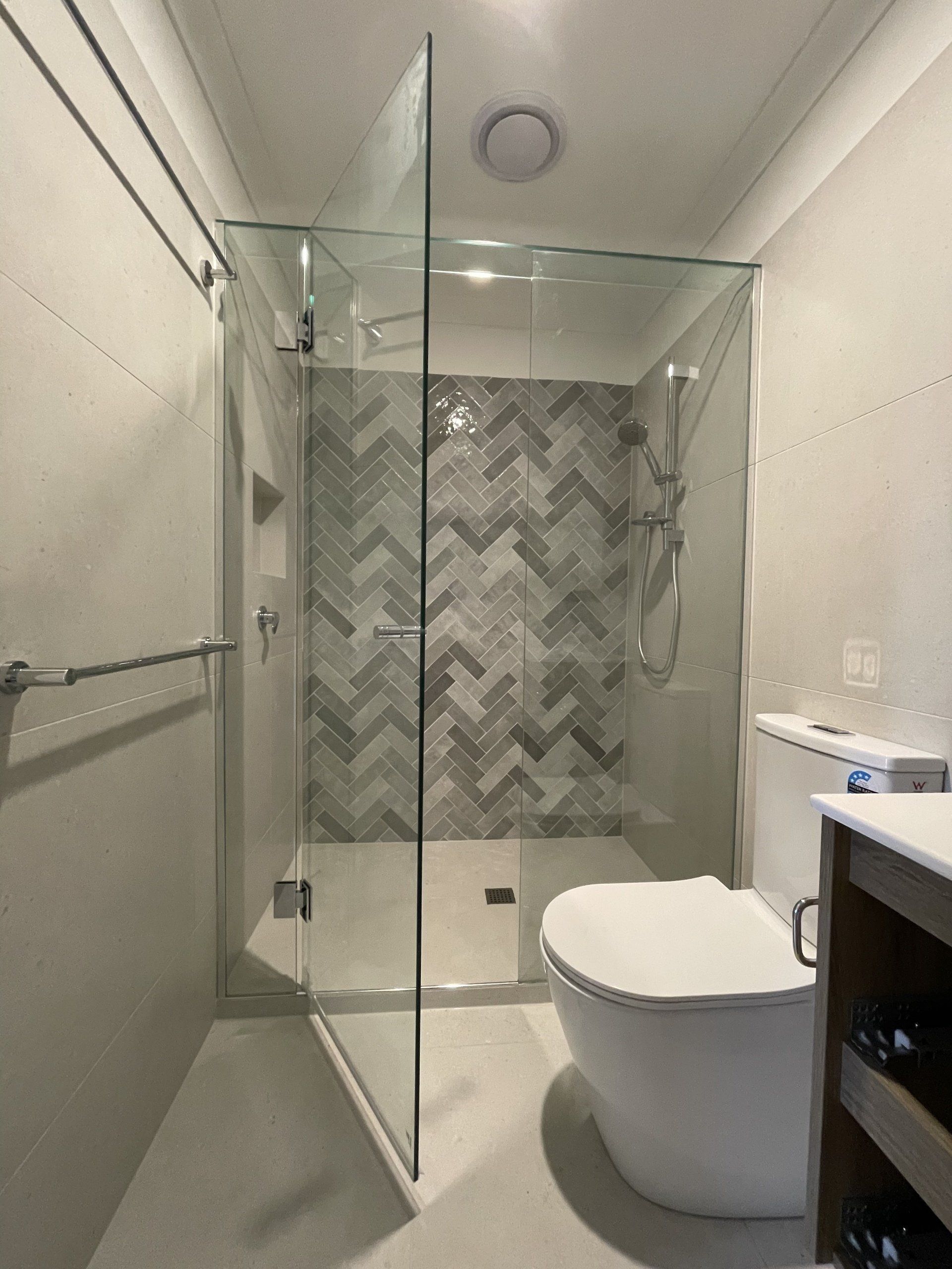 A bathroom with a toilet and a walk in Frameless Hinged Shower Screen.