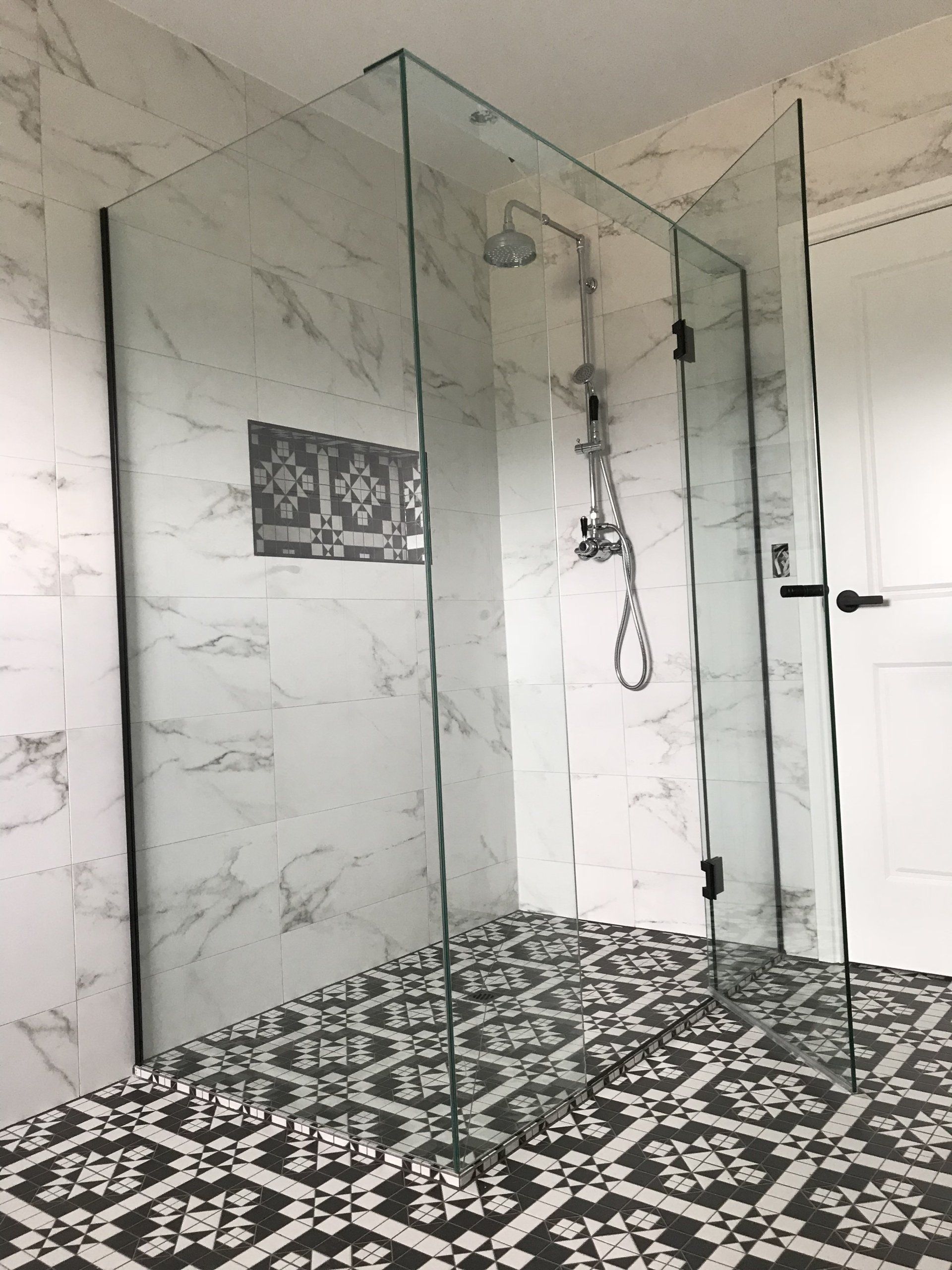 A bathroom with a walk in shower and a black and white tile floor.