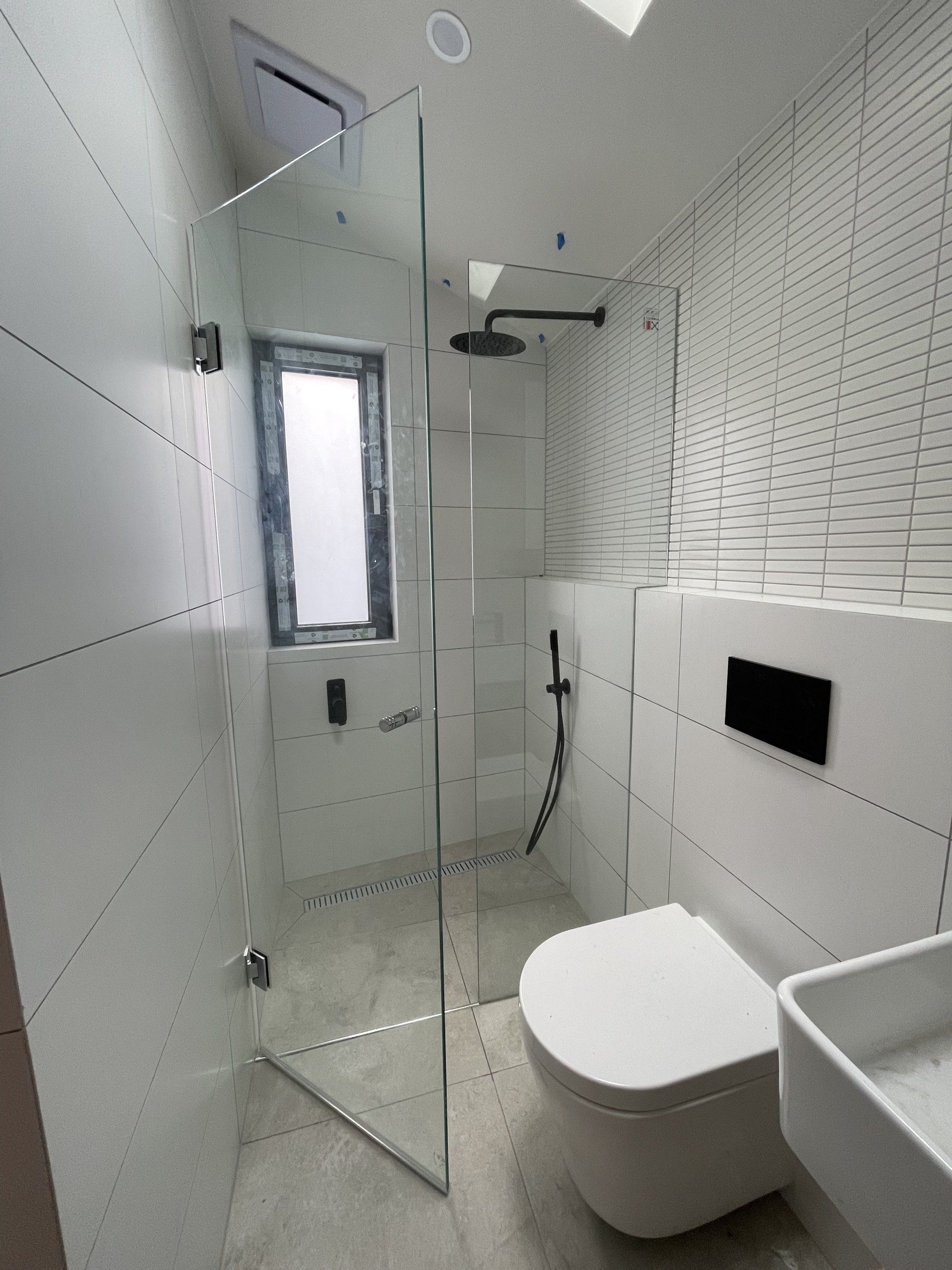 A bathroom with a toilet a sink and a walk in Frameless Hinged Shower Screen