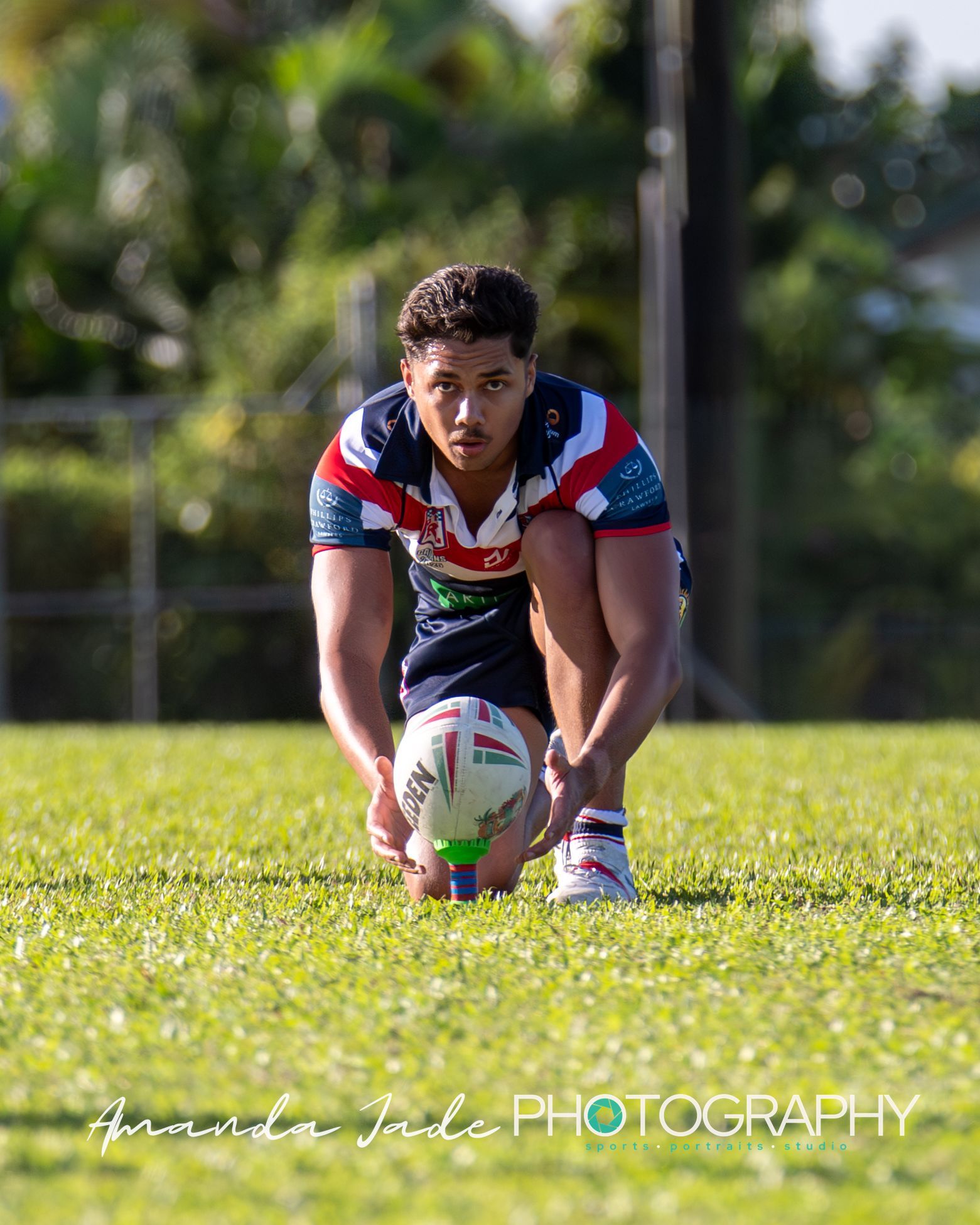 Man Kneeling On A Grassy Field, Preparing To Kick A Rugby Ball — Amanda Jade Photography In Gordonvale, QLD