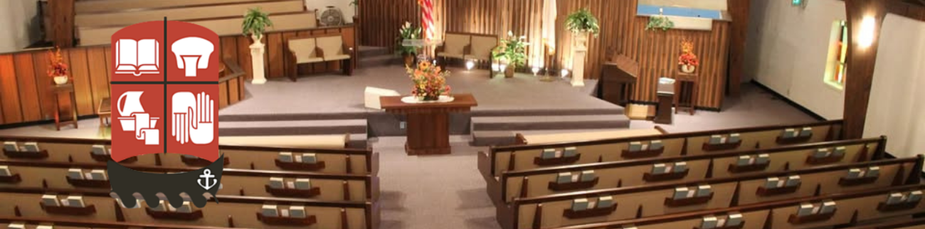 Empty church sanctuary with wooden pews facing a central altar and pulpit, warm lighting, and floral decor