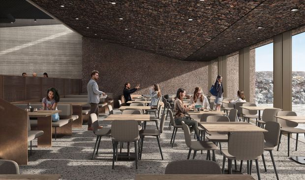 Cafe interior with people seated at tables. Stone wall and ceiling, large windows with outdoor view.