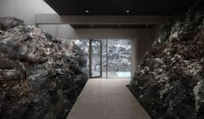 Hallway flanked by dark, textured rock walls, leading to a glass door revealing a pool and outdoor view.