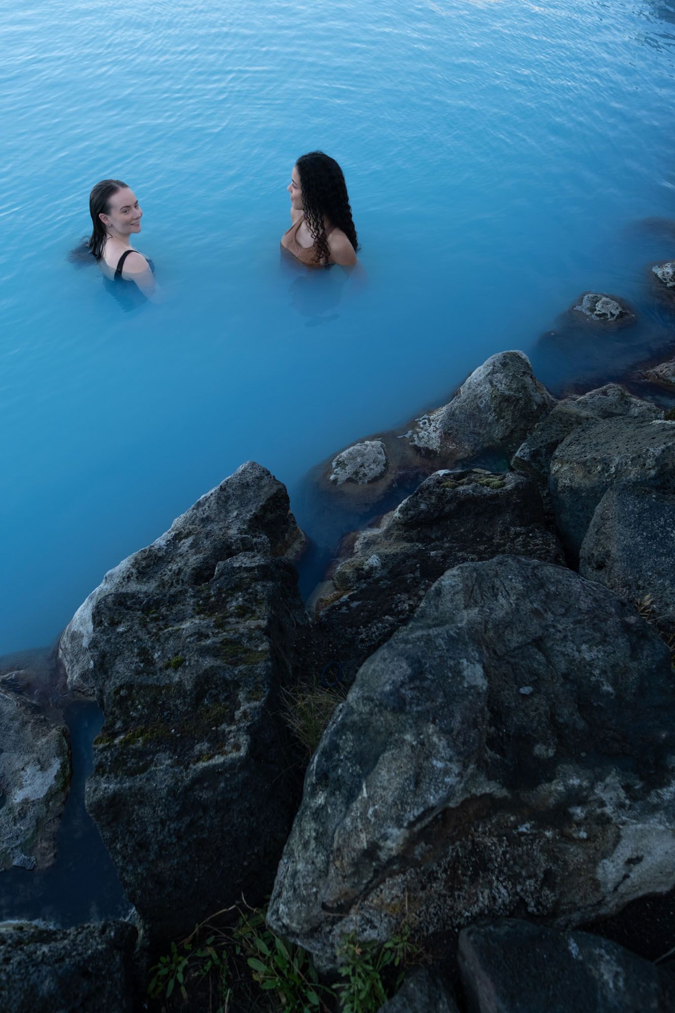 Jarðhitastöð með tyrkisbláu vatni, nútímaleg steinbygging og baðandi maður.