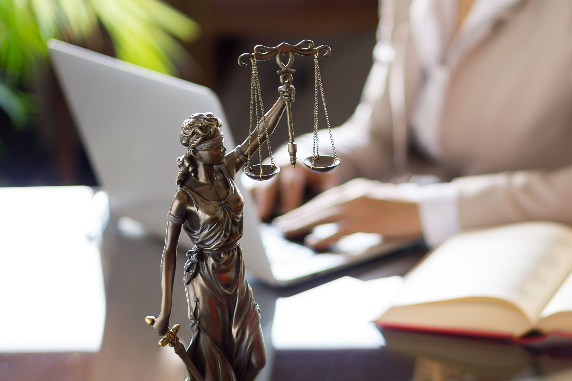 A statue of lady justice and a female attorney working on a laptop