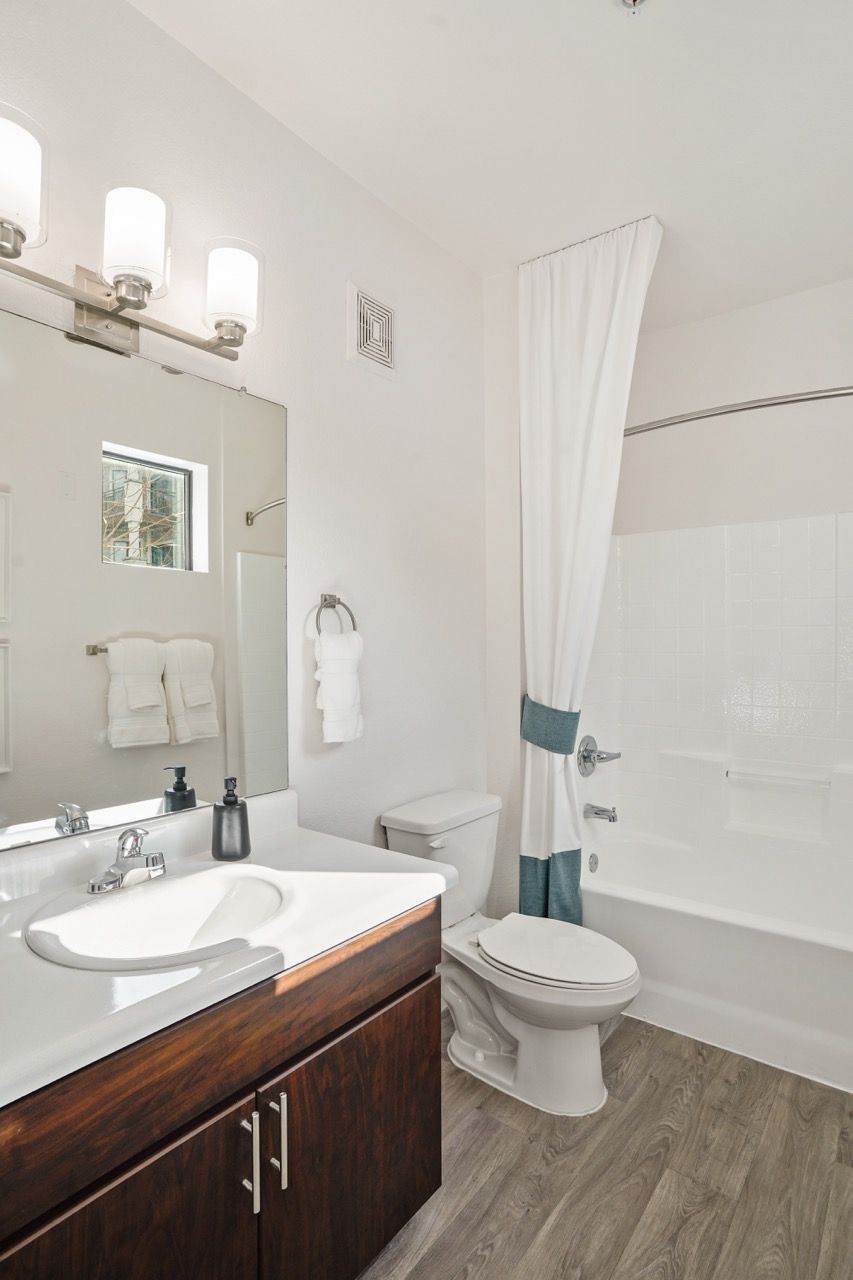 Modern bathroom with white sink, dark wood vanity, toilet, and bathtub with a white shower curtain.