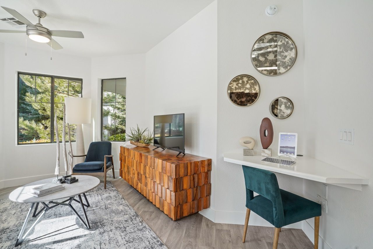 Bright apartment living area with a wooden block media console, blue chair, desk, and round wall mirrors.
