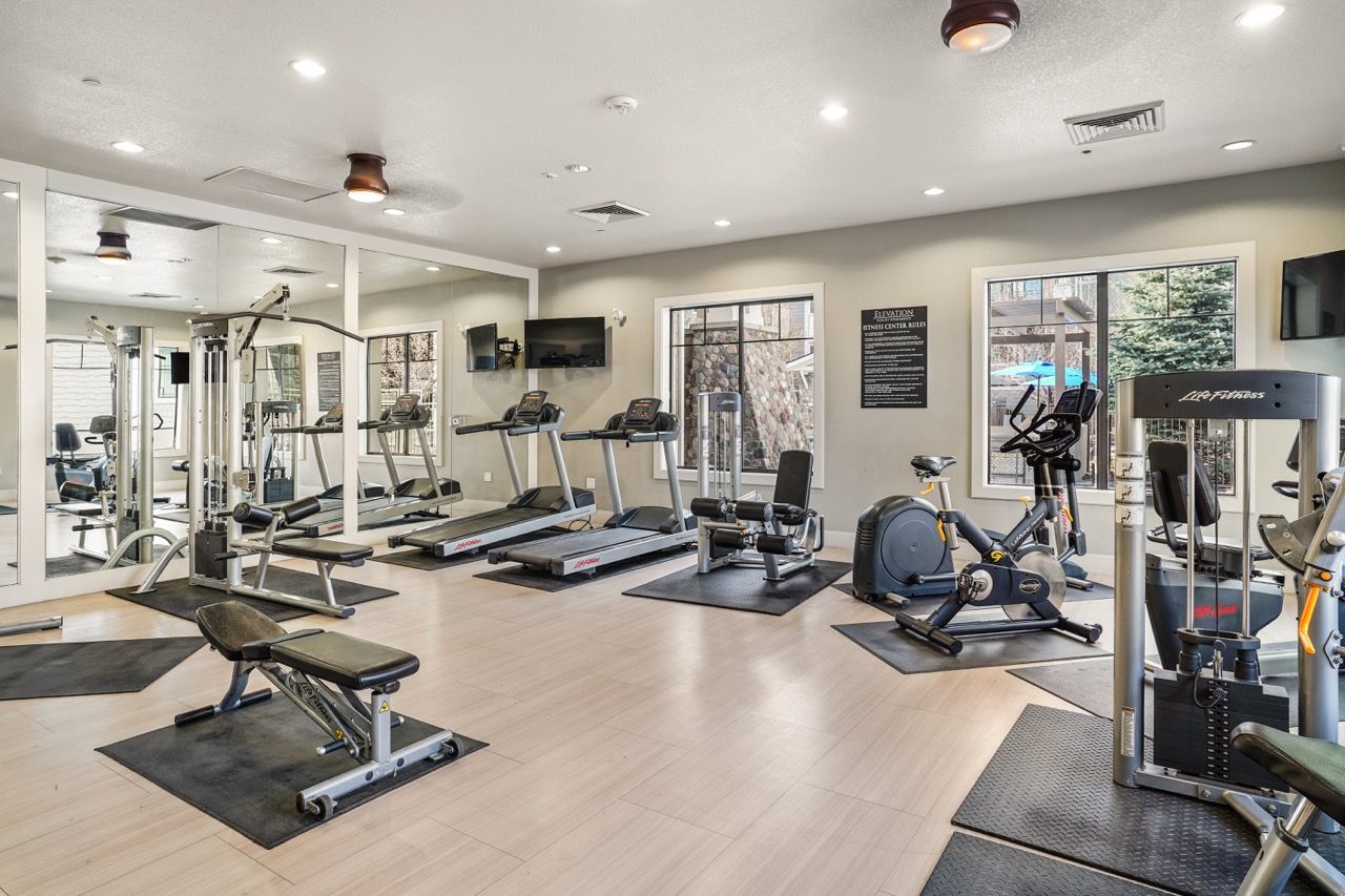 Well-lit apartment community gym with treadmills, bikes, and weight machines.