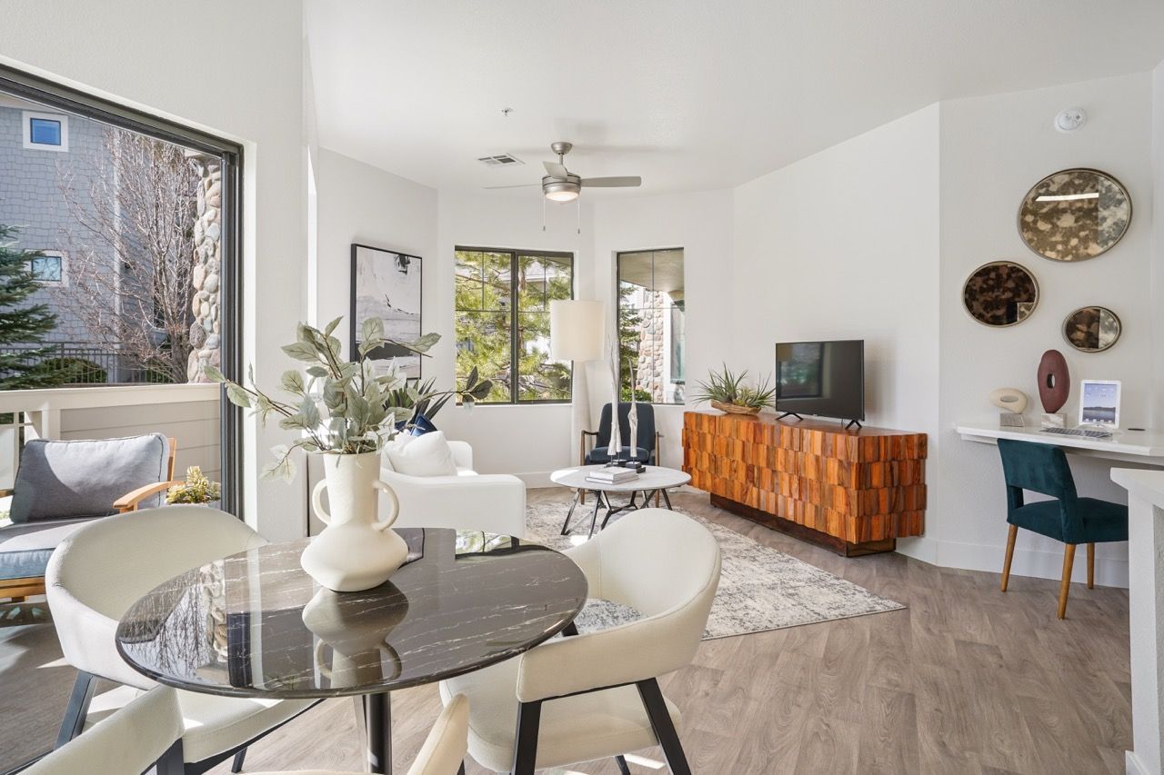 Bright apartment living room with white furniture, round marble table, and a wood-toned TV console.