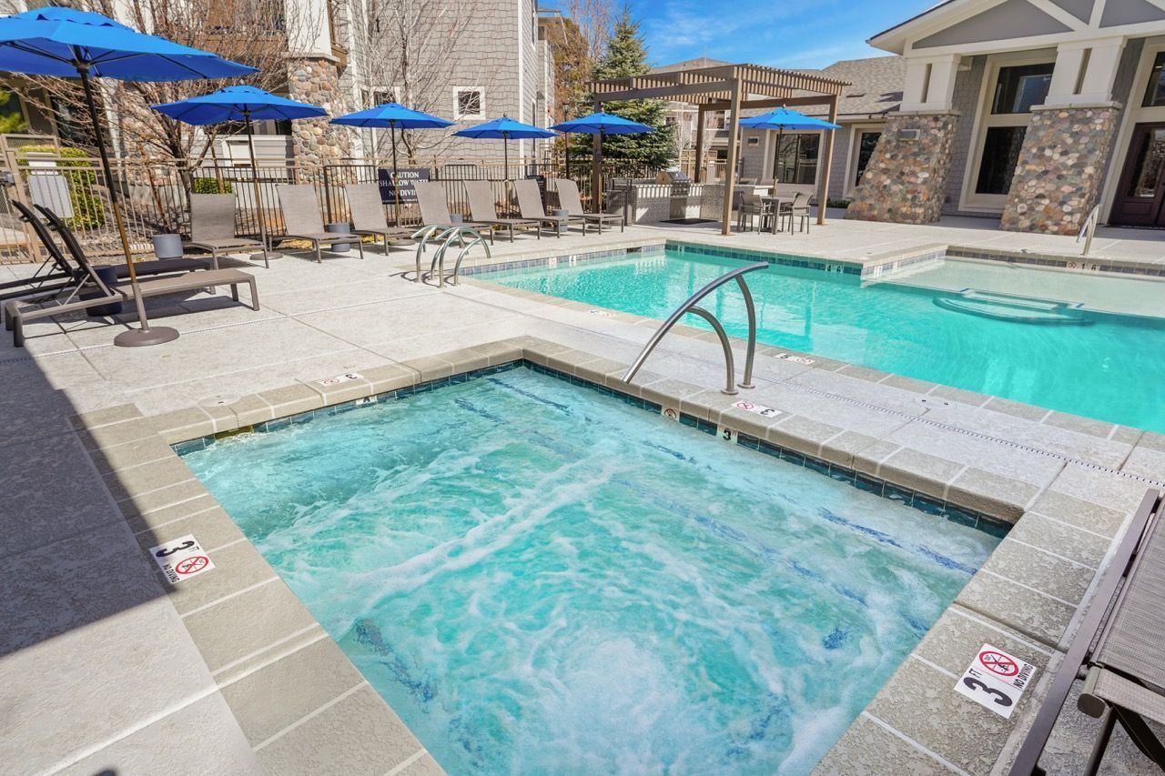 Outdoor pool and hot tub area with lounge chairs and blue umbrellas.