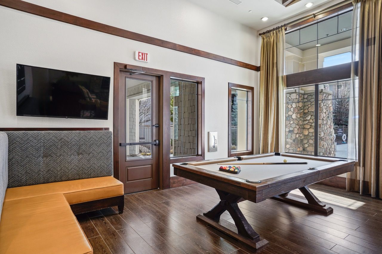 Indoor community lounge with a pool table, mounted TV, and large windows.