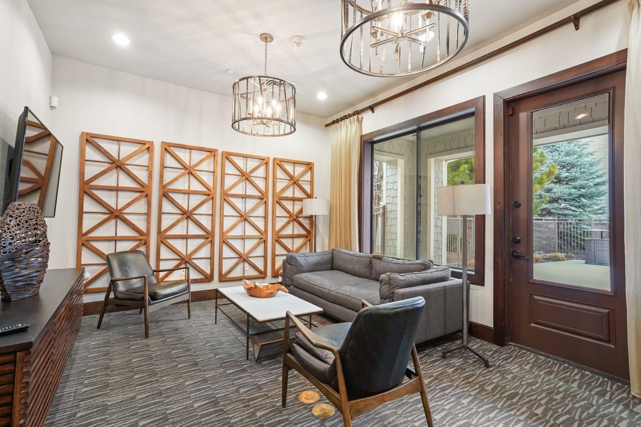 Interior community lounge with a gray sectional, chairs, coffee table, and wooden lattice screens by glass doors.