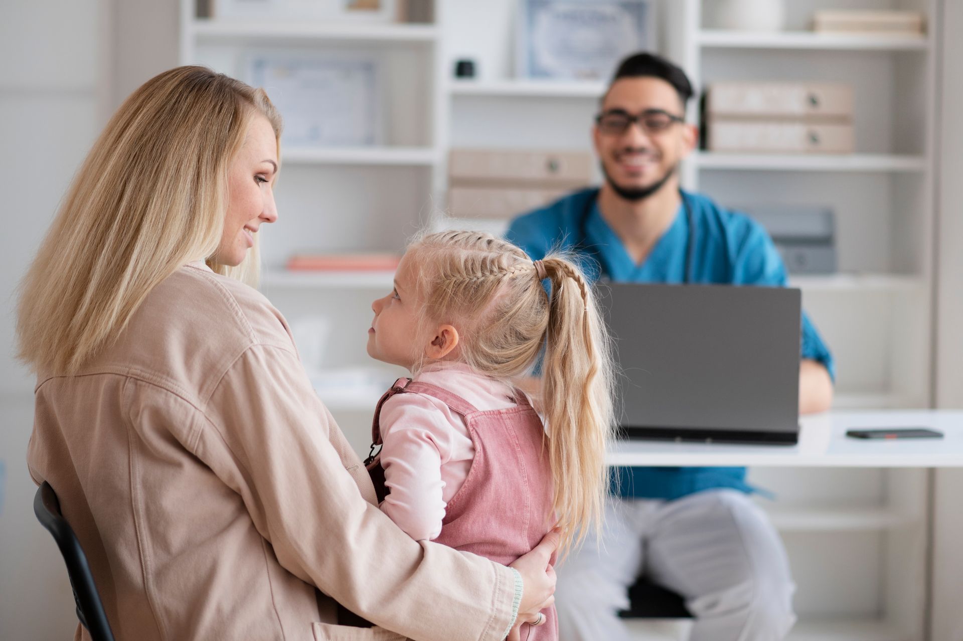 A woman is holding a little girl while talking to a doctor.