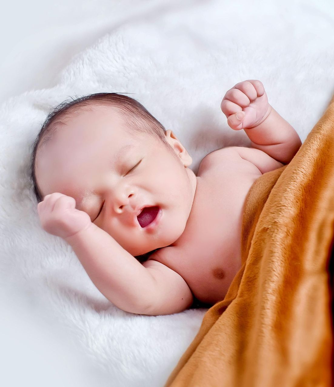 A baby is sleeping on a bed with his mouth open.