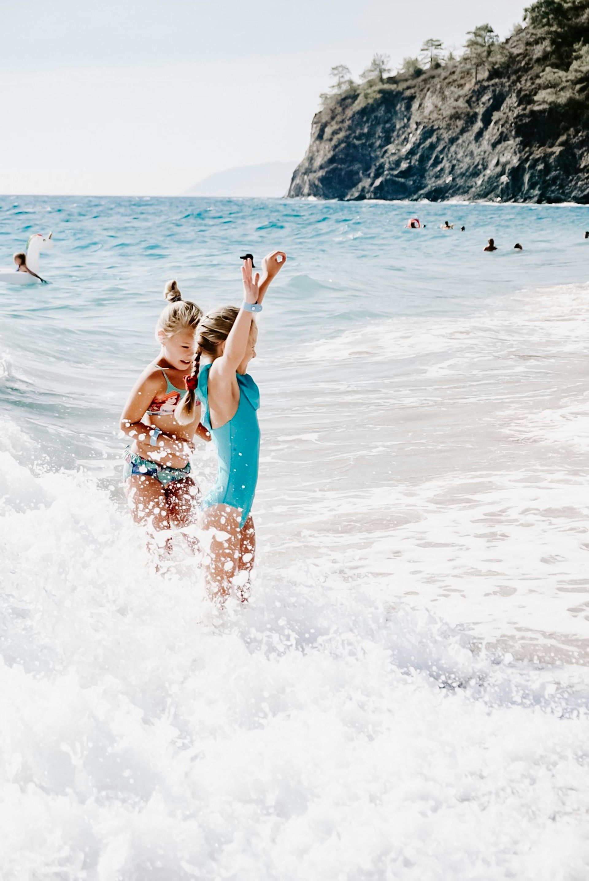 Two young girls are playing in the ocean with mountains in the background.