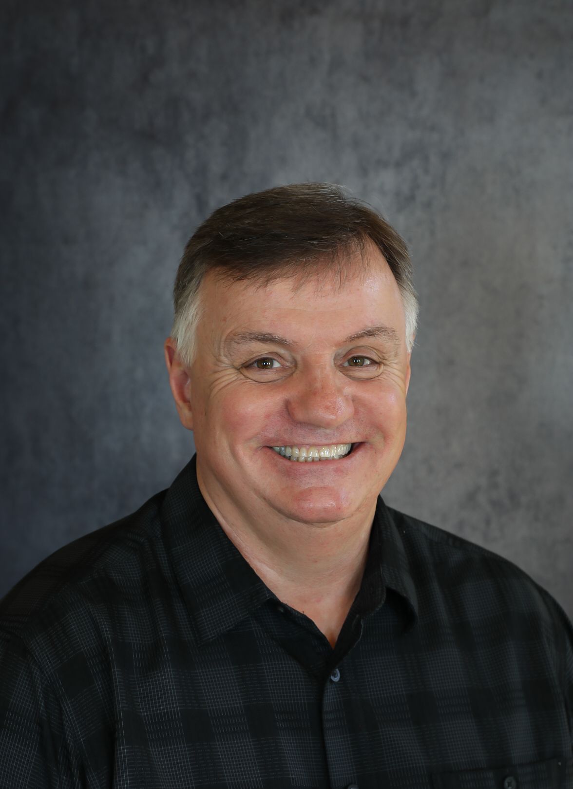 Epp Walls smiling in a black patterned shirt against a gray background.
