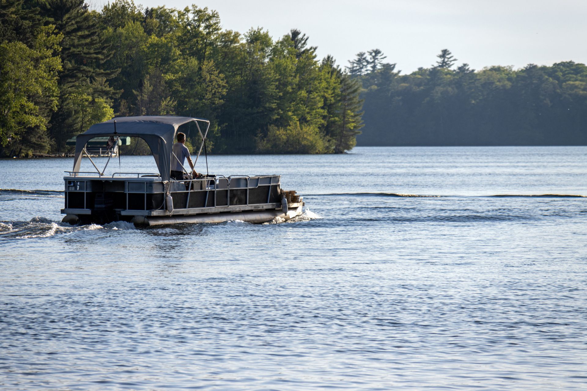 Pontoon boat on a lake with a dark blue canopy and a treeline in the background.