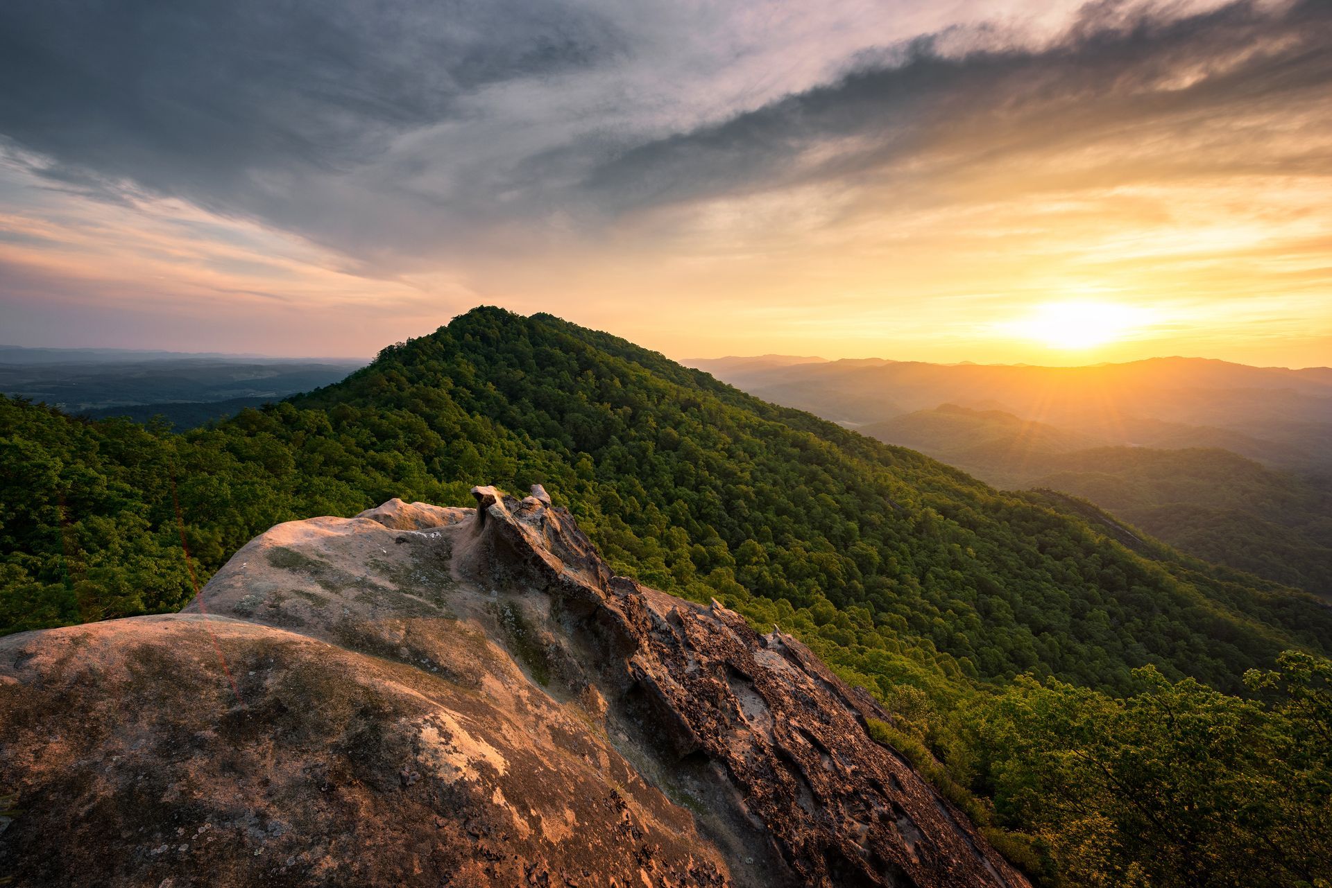 Sunset over a green mountain ridge with a rocky outcrop in the foreground.