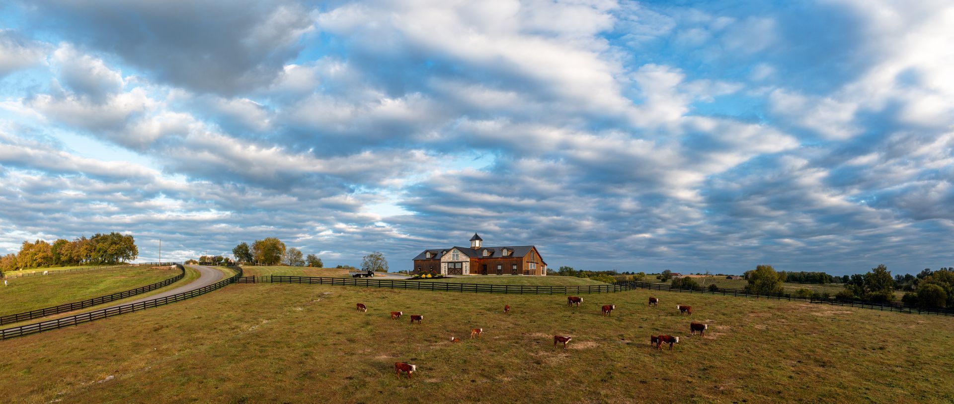 A large brick building on a grassy hill under a cloudy sky. A winding road leads to the building.