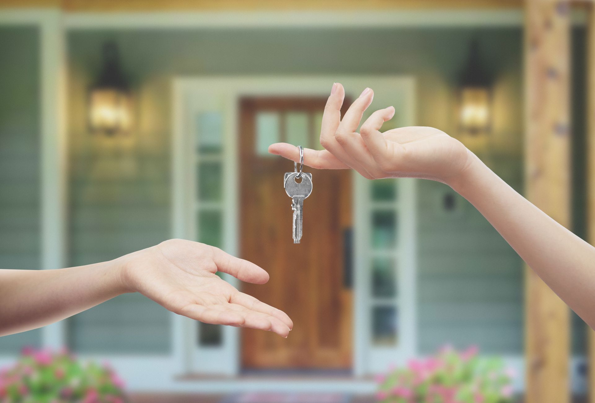 Hands exchanging house keys in front of a house entrance.