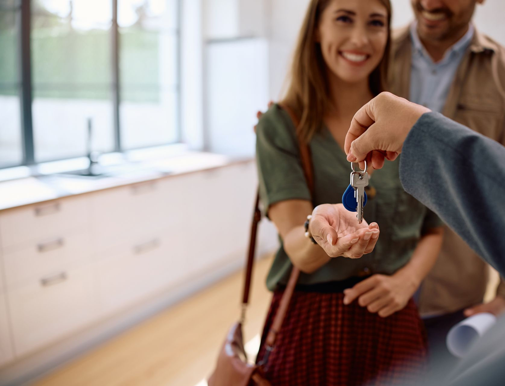 Person handing keys to smiling woman in a new home. Man in background.