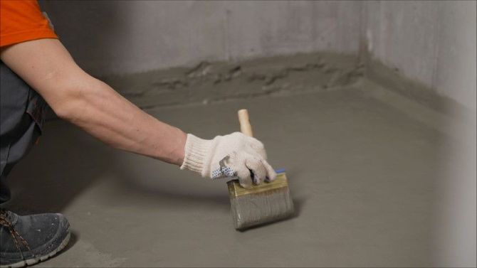 Person in work gloves brushing gray concrete on a floor with a paintbrush