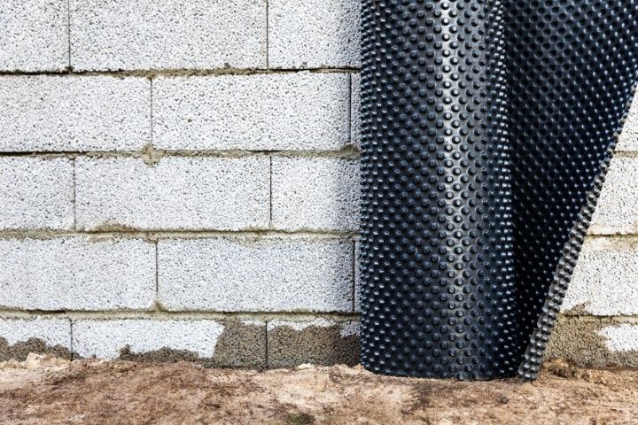Black drainage board against a cinder block wall with dirt at the base