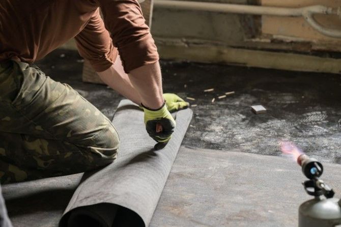 Person measuring a rolled sheet in a workshop, with a small torch nearby